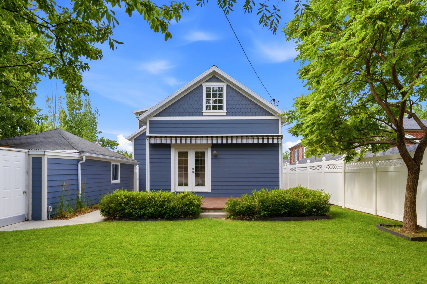 Rear exterior featuring blue siding, white double French doors, a striped awning, and a gabled dormer window