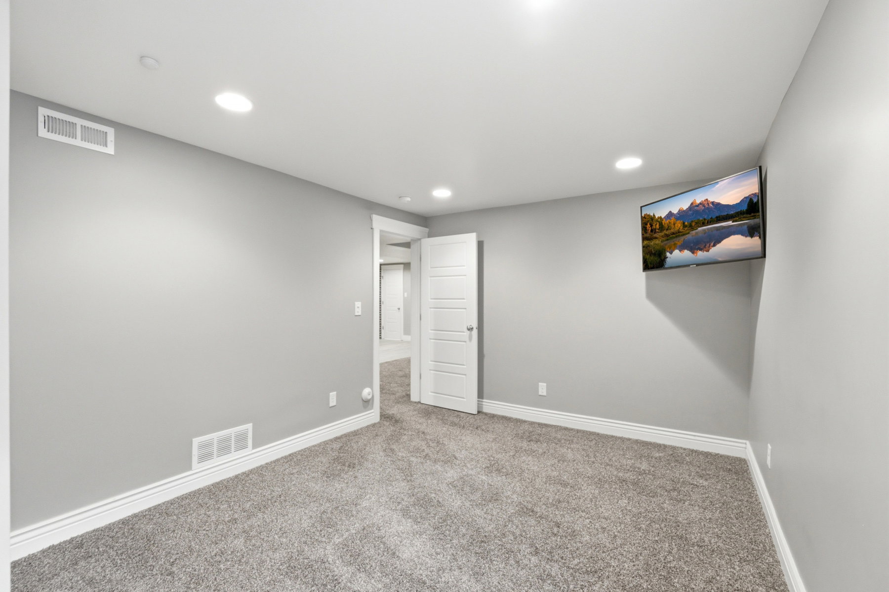 Spacious room featuring neutral gray walls, recessed lighting, white baseboards, and plush gray carpeting