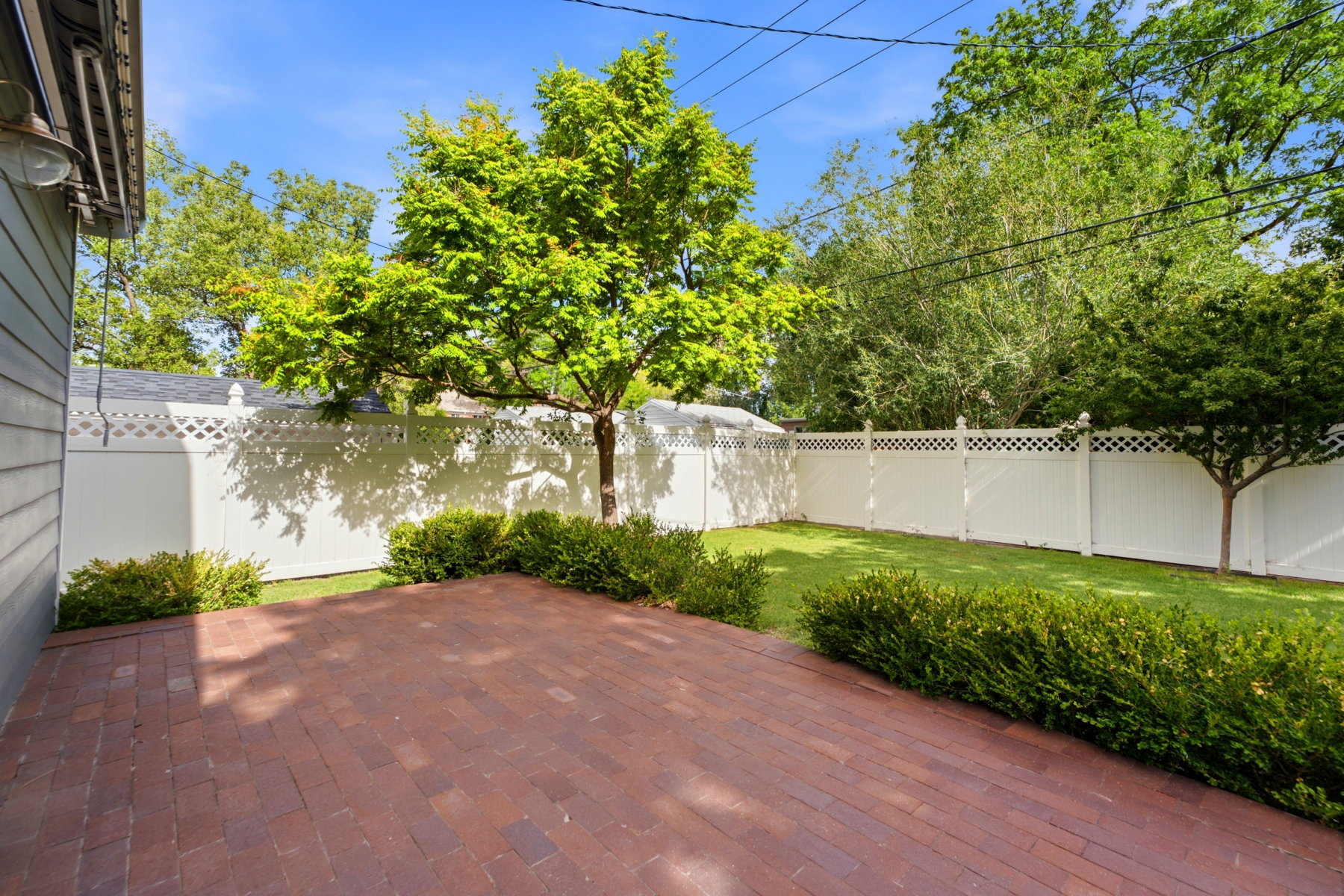 Expansive brick paver patio bordered by established shrubbery