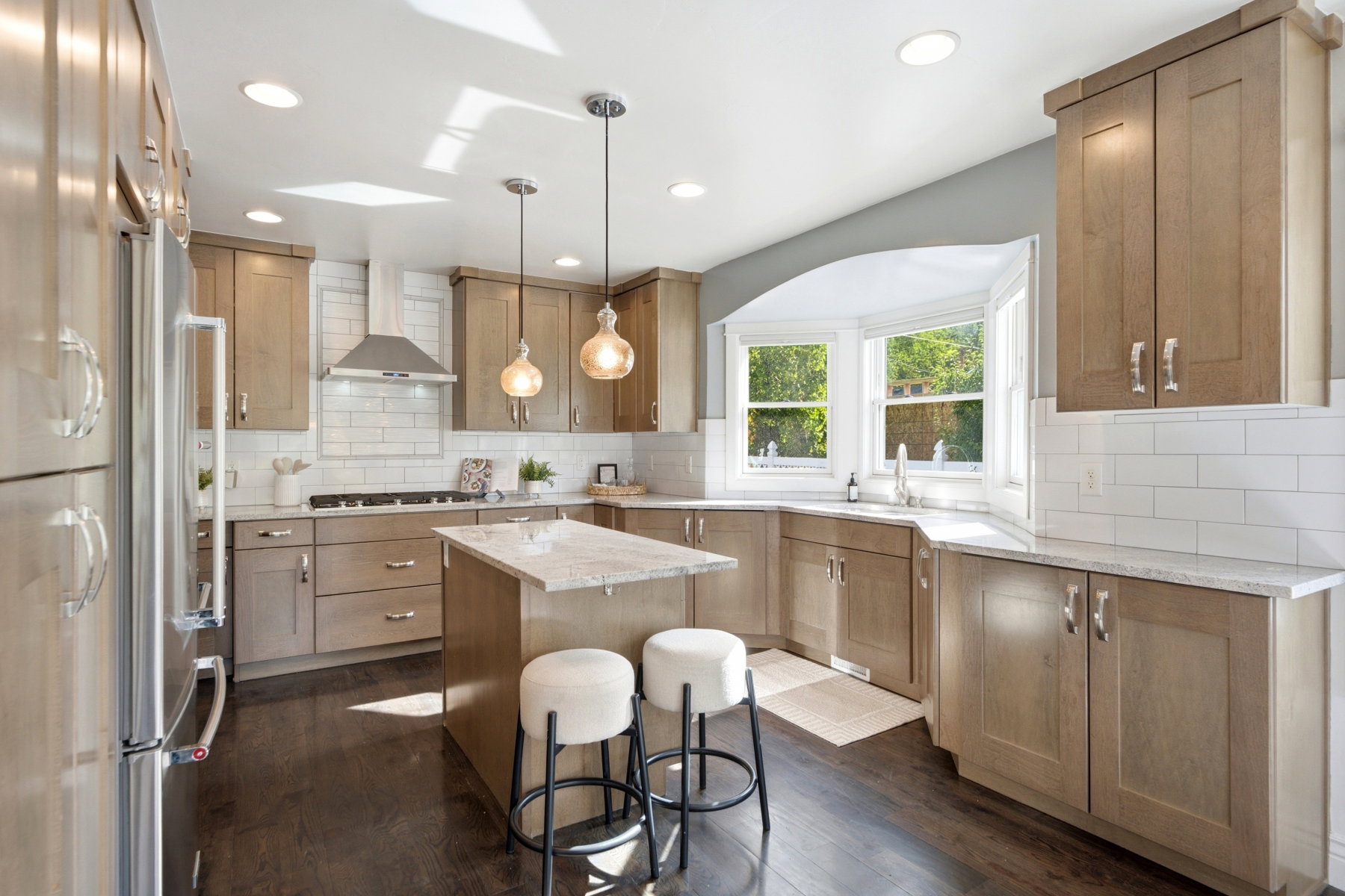 Modern kitchen featuring light wood-finish cabinetry, stainless steel appliances, a center island with a light-toned countertop, and a bay window