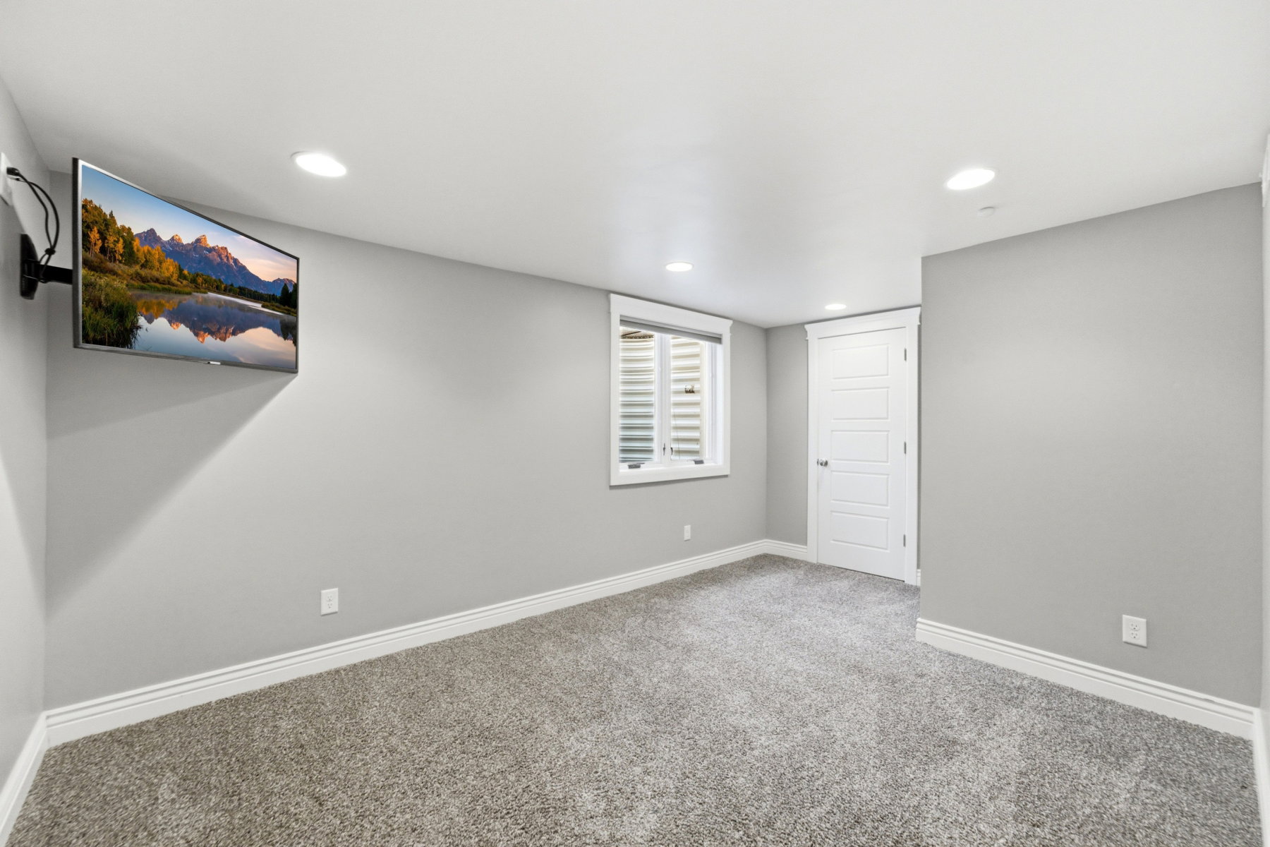 Carpeted room featuring recessed lighting, a mounted television, a window with plantation shutters, white trim, and a paneled door