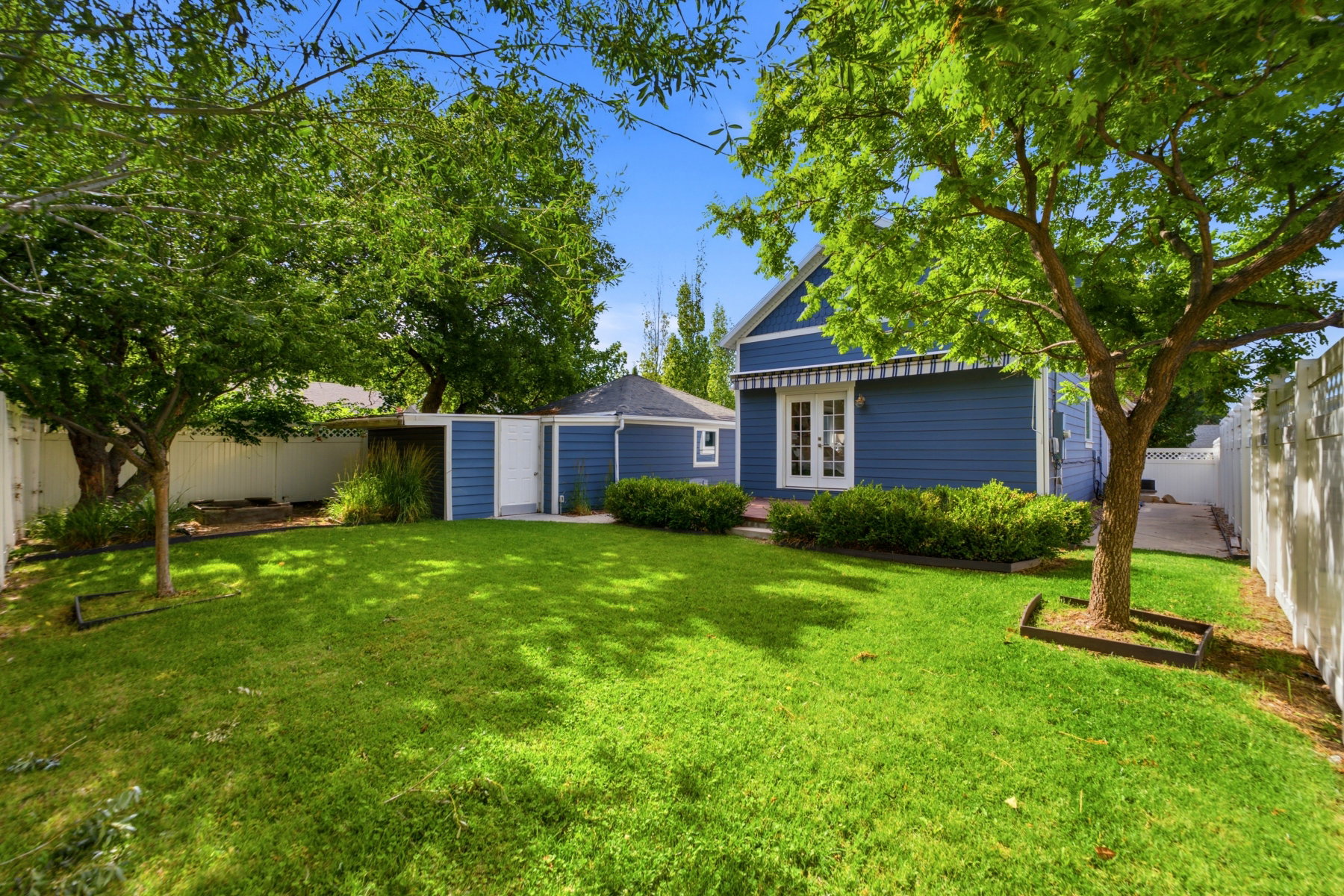 Expansive green lawn with mature shade trees, white privacy fencing, and a detached structure