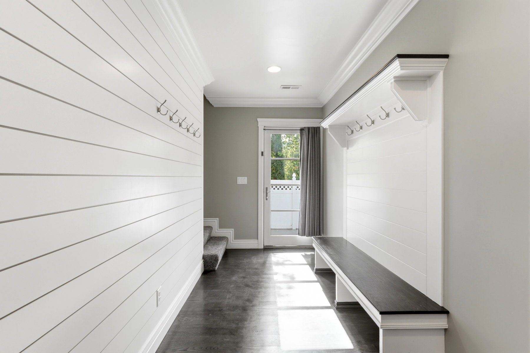 Entryway mudroom featuring shiplap walls, built-in bench with dark wood-finish top, integrated coat hooks, and crown molding
