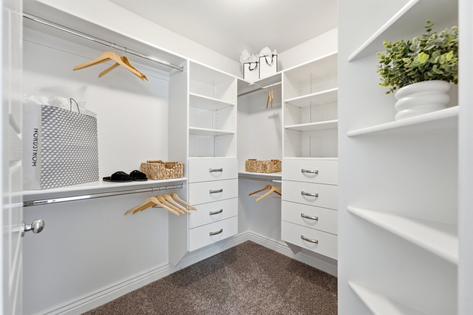 Walk-in closet featuring built-in white shelving, integrated drawers with polished chrome hardware, and multiple hanging rods