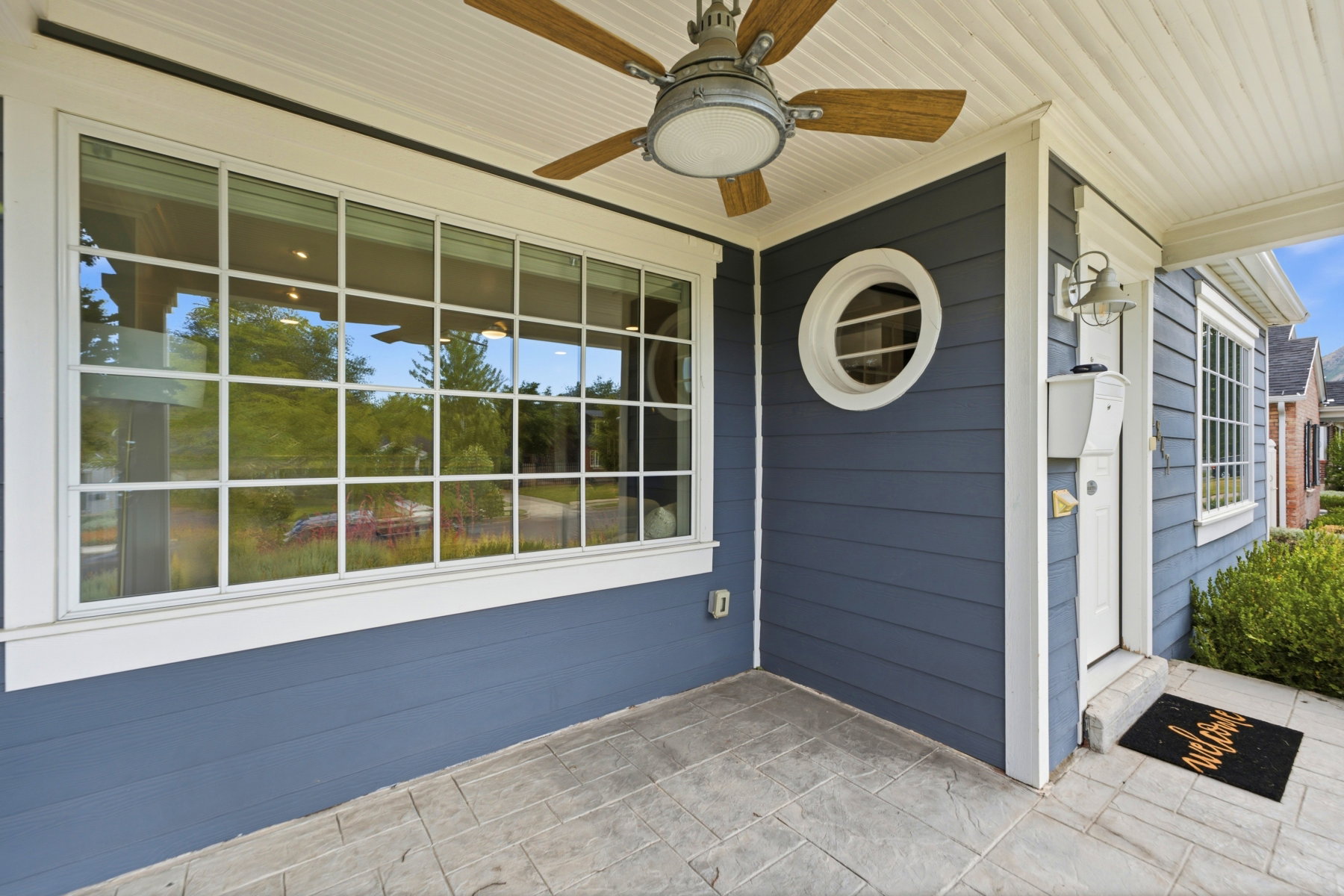Covered porch featuring stamped concrete flooring, a ceiling fan with wood-finish blades, board and batten siding, a prominent multi-pane window, and a circular accent window