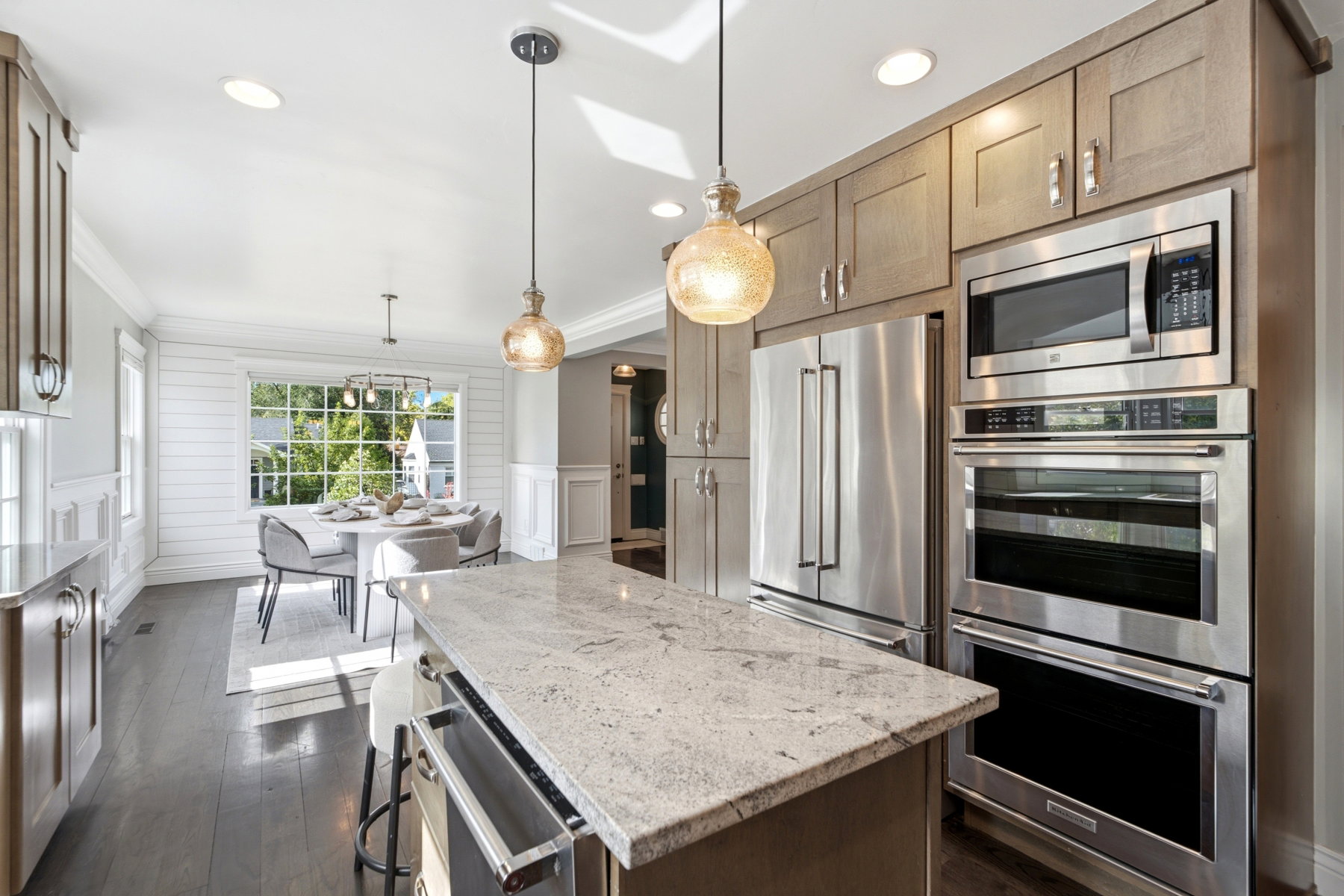 Open-concept kitchen featuring an oversized island with a stone countertop, stainless steel appliances, wood-finish flooring, recessed lighting, and pendant fixtures