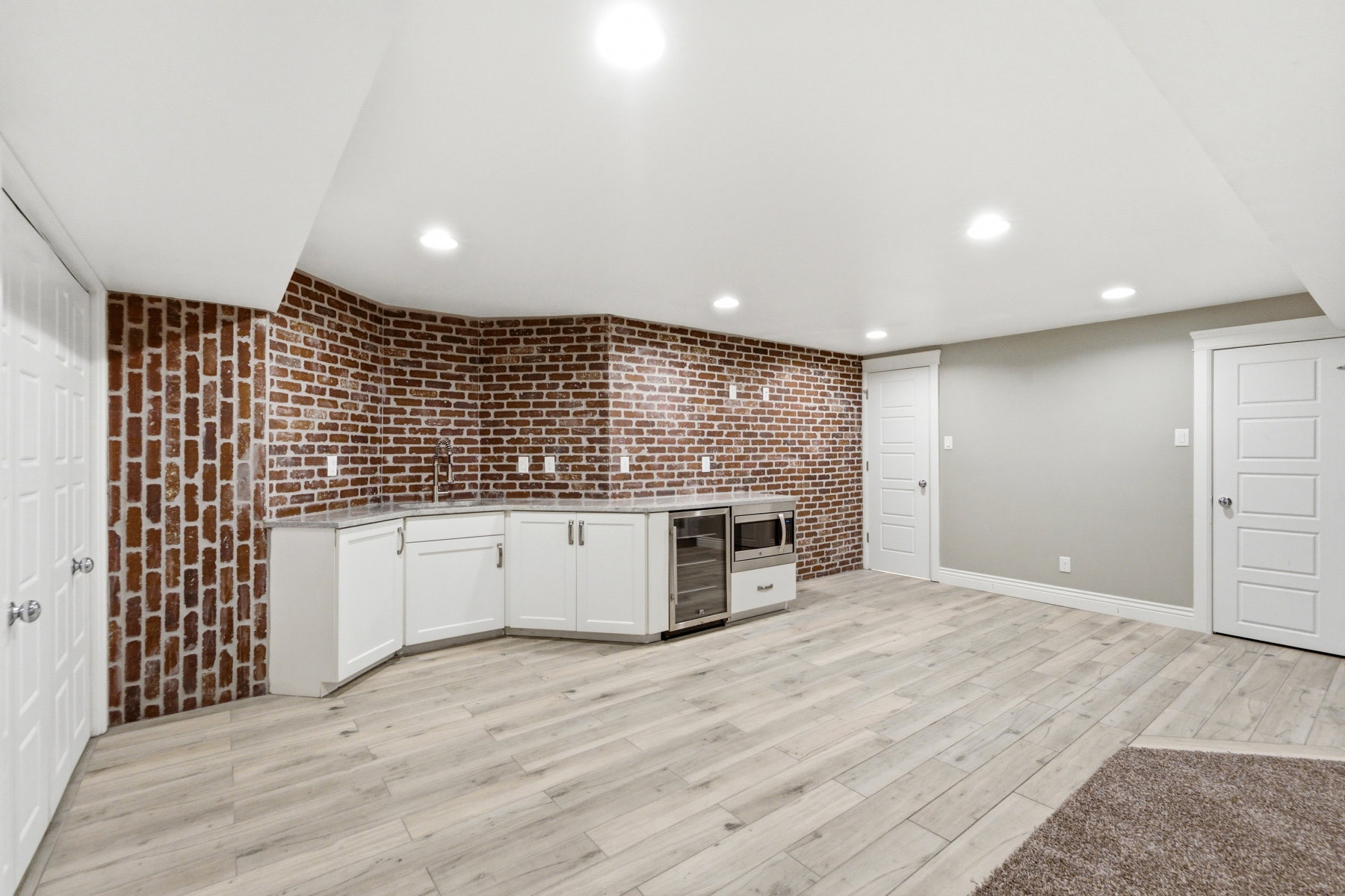 Brick accent wall with white cabinetry and light wood-finish flooring
