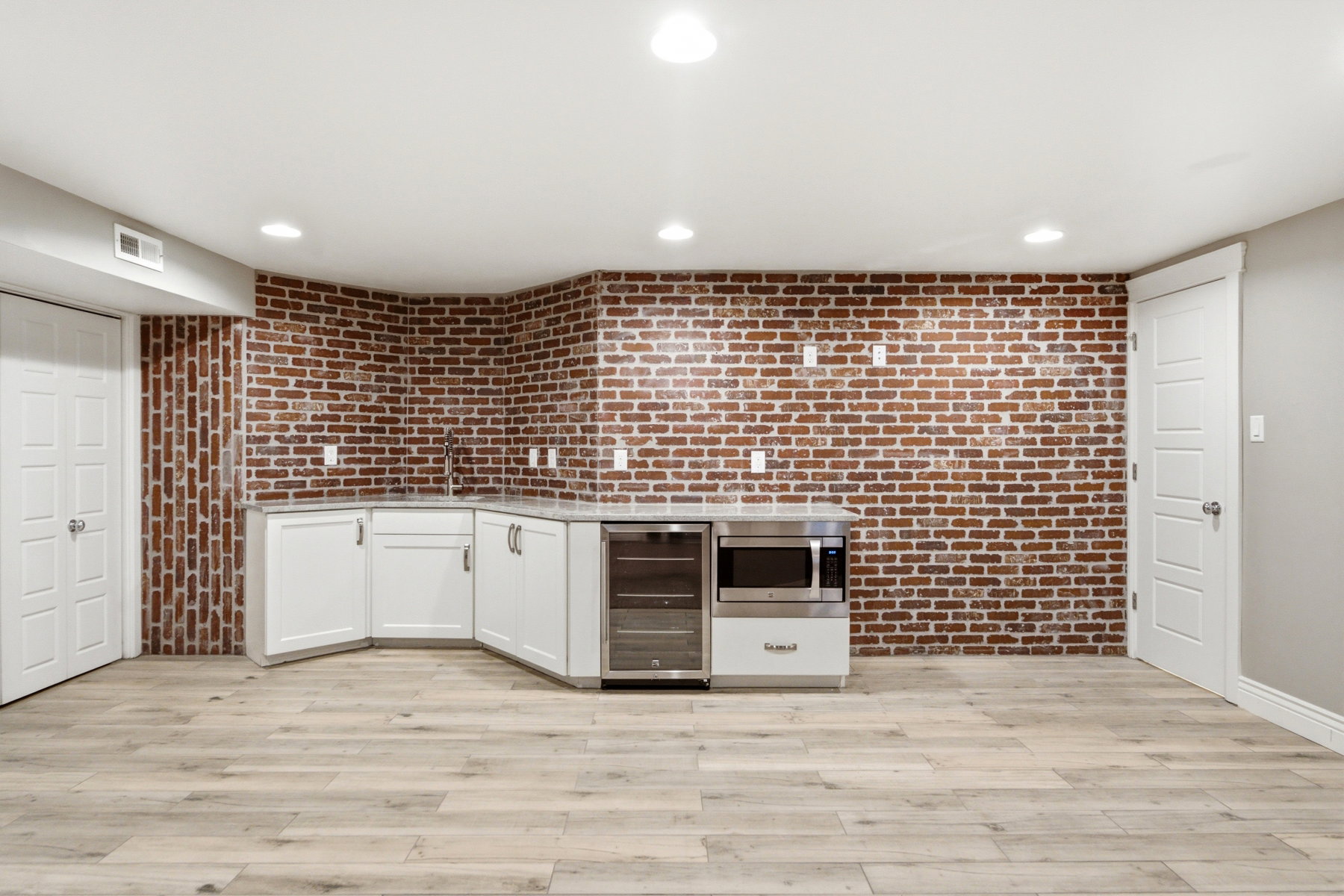 Entertainment area featuring an exposed brick wall accent, light wood-finish flooring, white cabinetry with a built-in microwave, beverage cooler, and recessed lighting