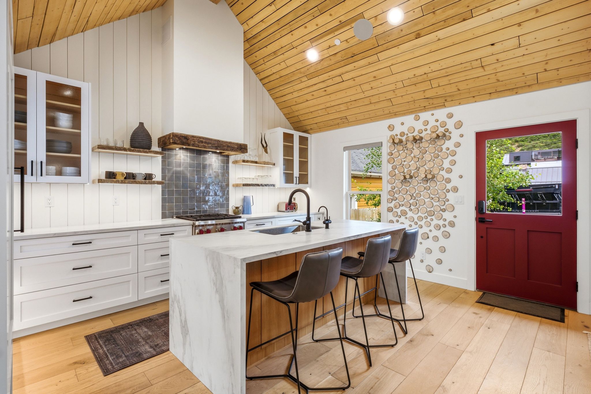Modern kitchen with a striking red door and a vaulted wood-plank ceiling