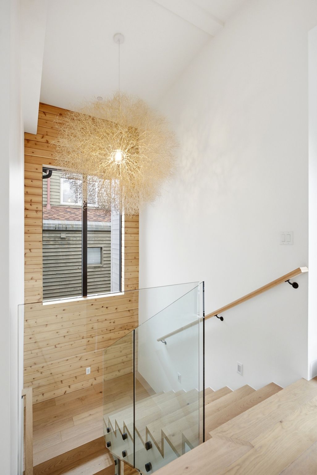 Stairwell featuring light wood-finish flooring and stairs, a glass panel railing, and a wood handrail