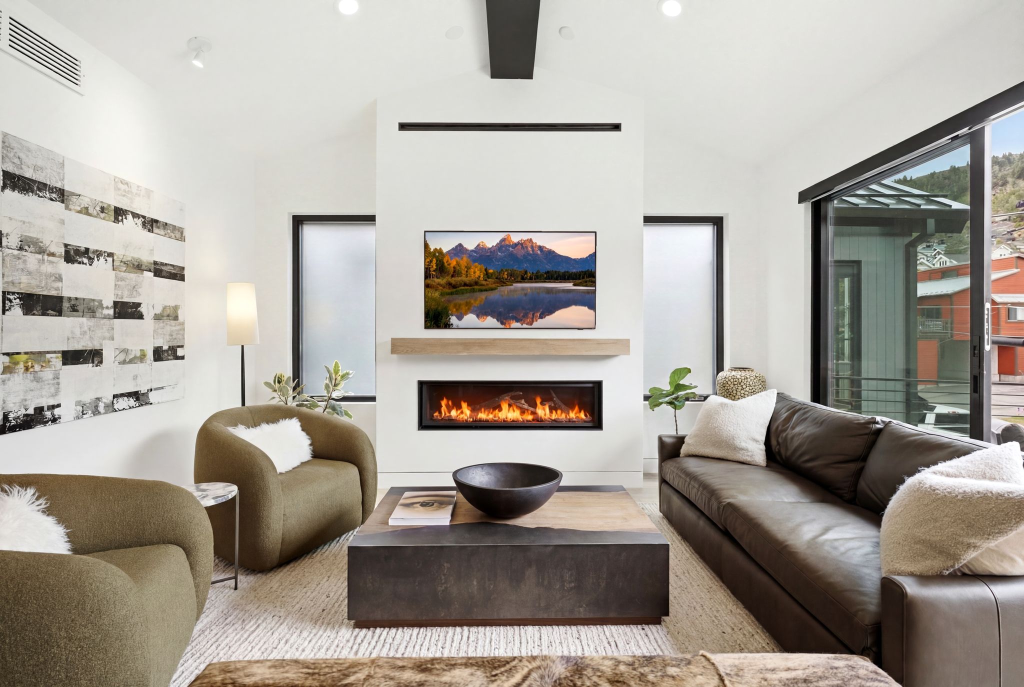 Living area featuring a sleek fireplace with a wood mantle, large format sliding glass doors, white walls, and wood-finish flooring