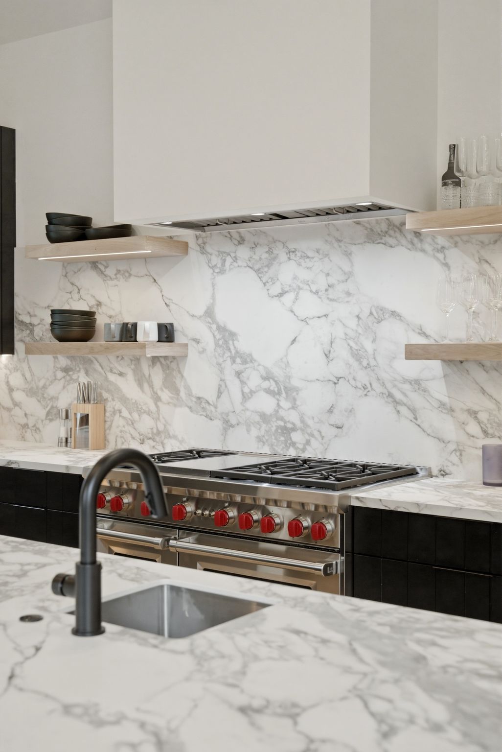 Gourmet kitchen featuring a professional-grade stainless steel range with red knob accents, a matching stainless steel range hood, and a full-height stone slab backsplash