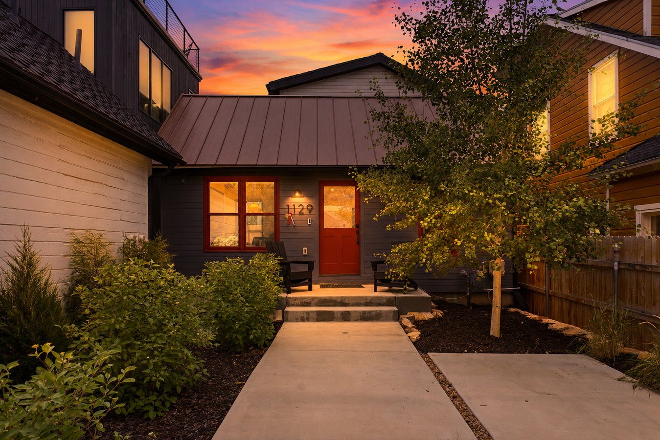 Modern facade with dark gray siding, a prominent red entry door, and red-trimmed windows
