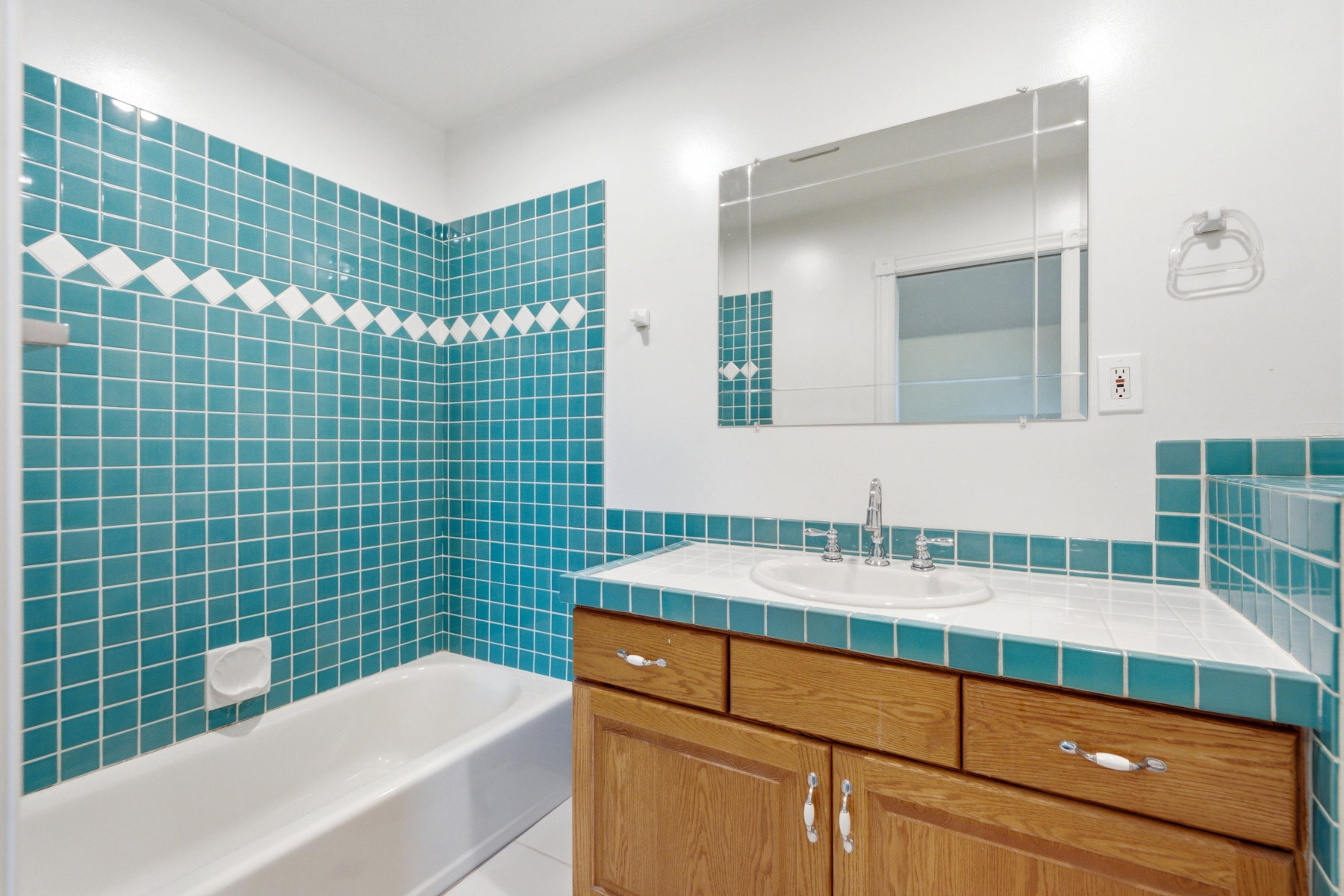 Bathroom featuring bright teal and white square tilework, a white porcelain bathtub, and a wood-finish vanity with a built-in sink