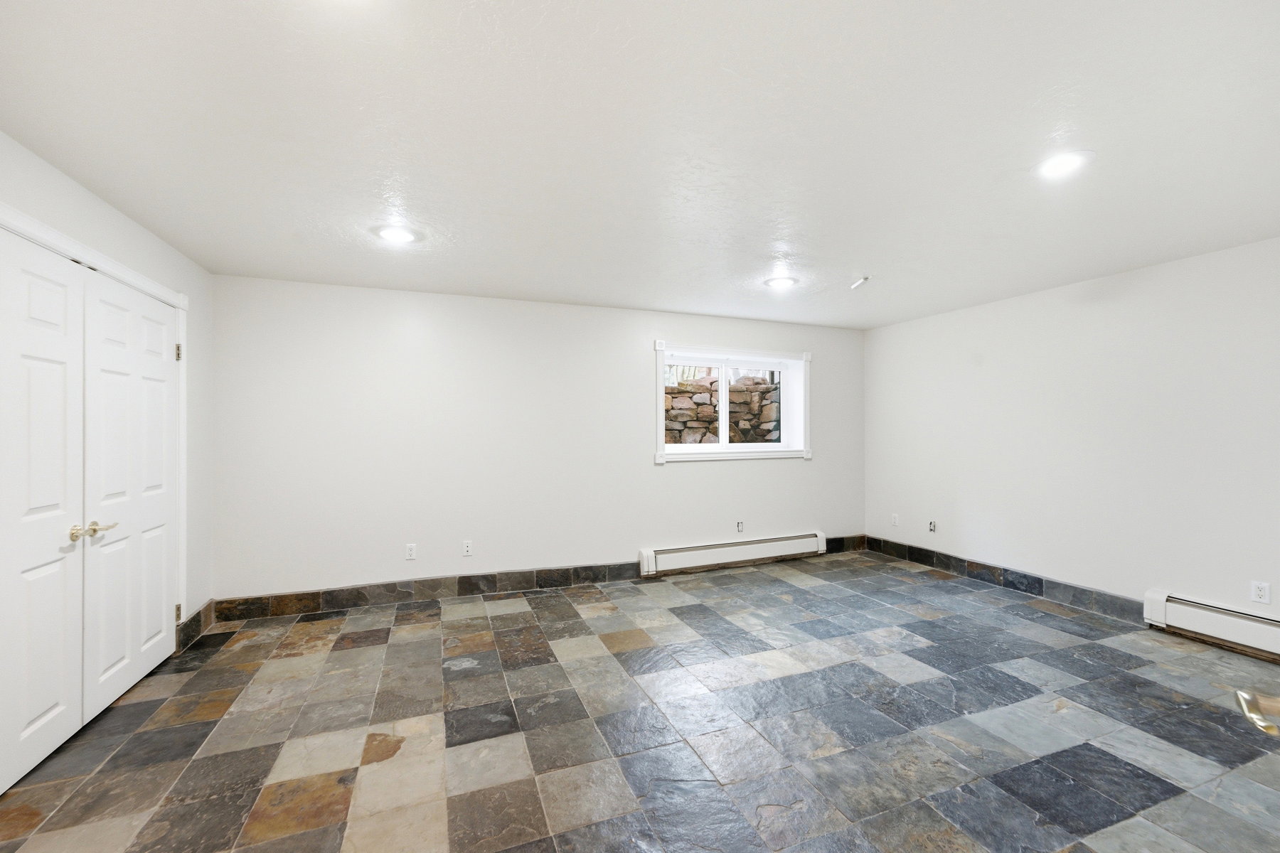 Spacious room featuring slate tile flooring, white walls, and a window with a stone well view
