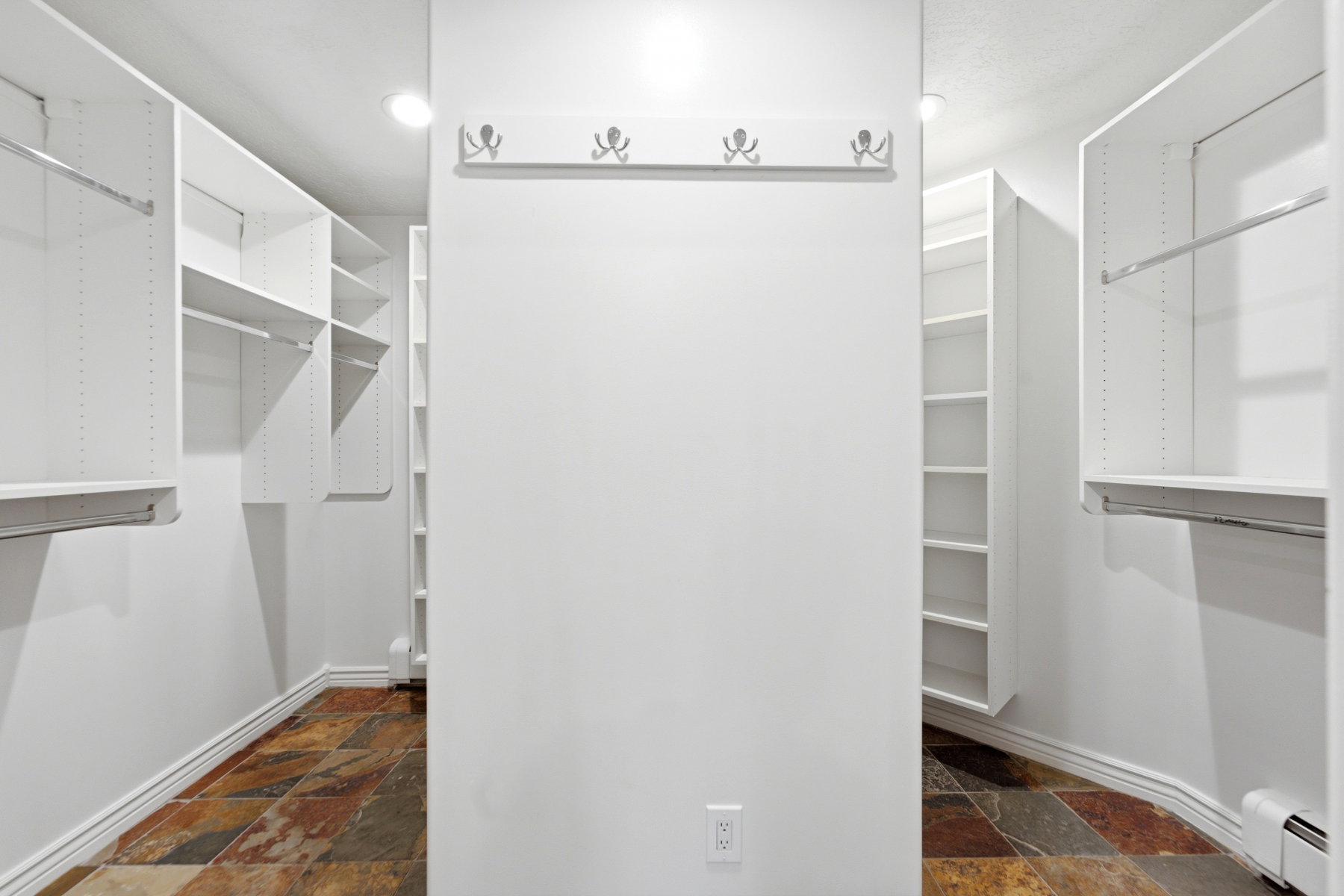 Walk-in closet featuring extensive built-in shelving, multiple hanging rods, recessed lighting, and multi-toned stone tile flooring