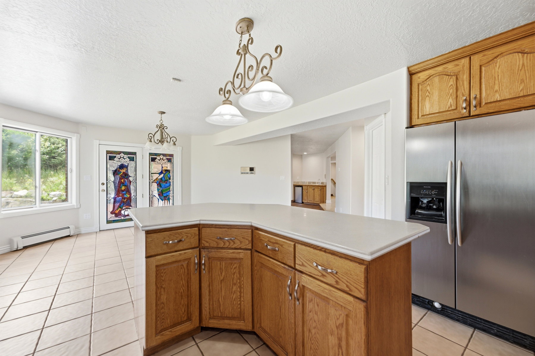 Open-concept kitchen featuring an angled island with ample storage, stainless steel refrigerator, and wood cabinetry