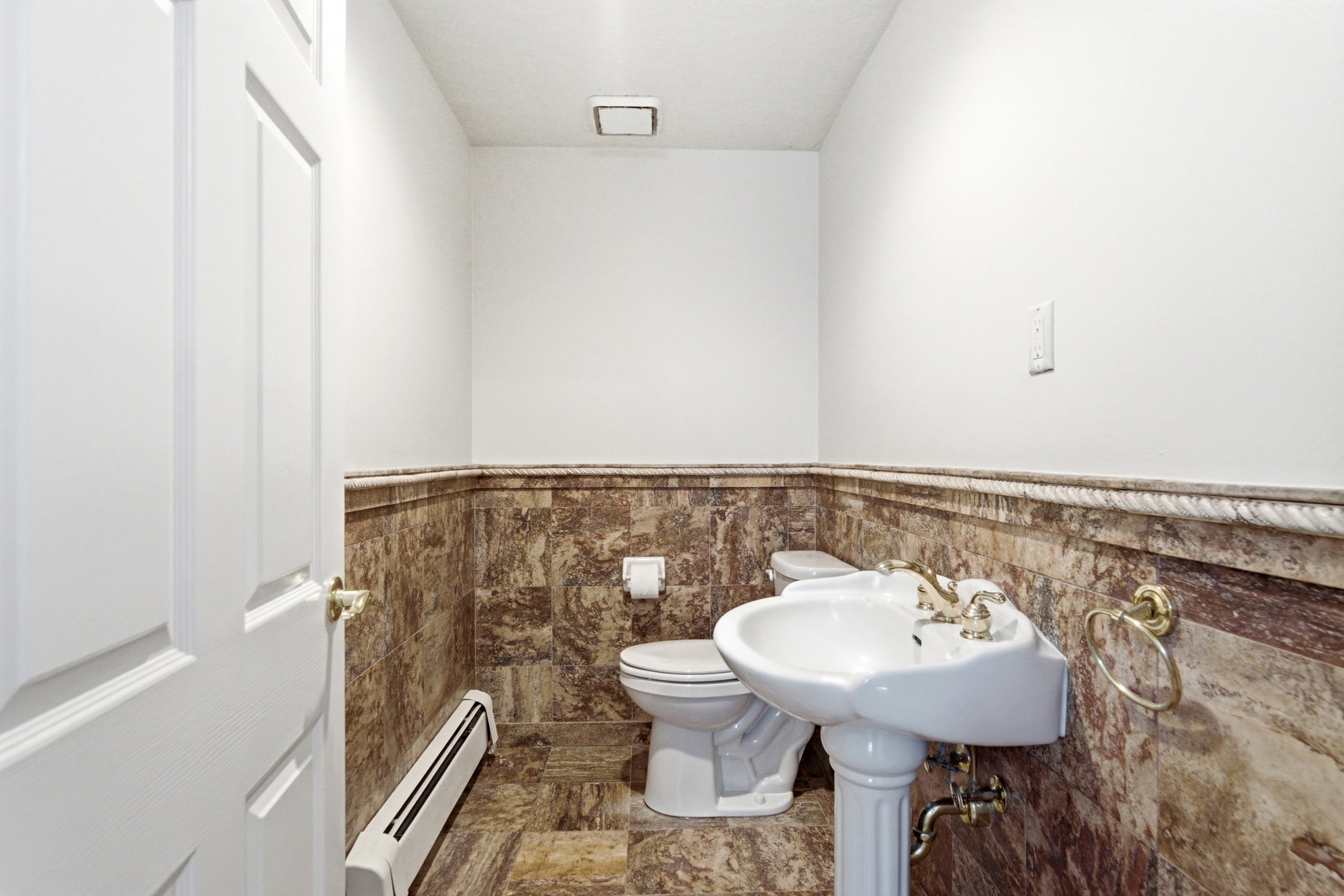 Pedestal sink with brass-finish faucet, toilet, and marble-look wainscoting