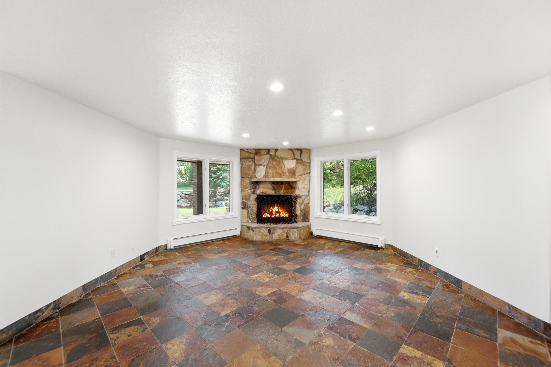Corner stone fireplace with a natural wood-burning fire, complemented by slate tile flooring