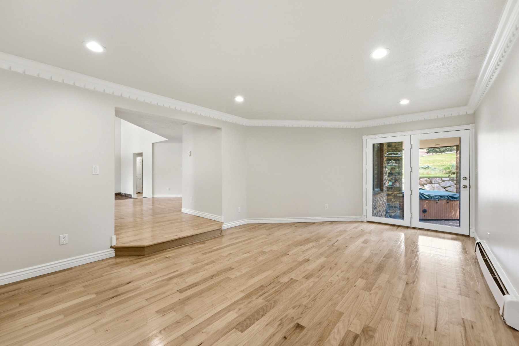 Expansive room featuring hardwood flooring, recessed lighting, decorative crown molding, and a double patio door providing outdoor access