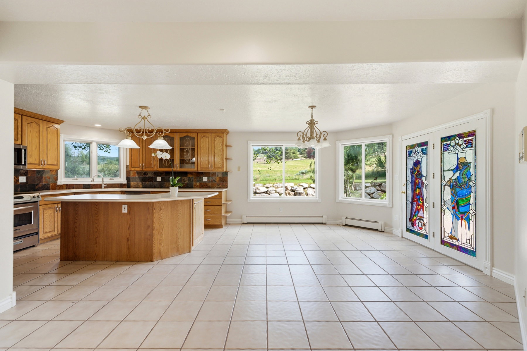 Expansive kitchen and dining area featuring light wood cabinetry, a central island with a light-toned countertop, and stainless steel appliances