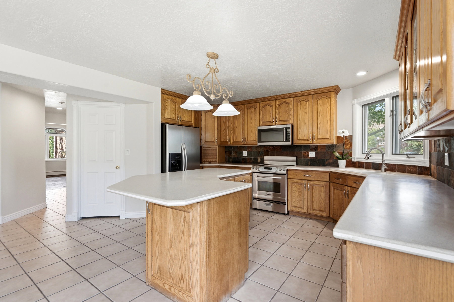 Kitchen featuring a central island with countertop, light wood-finish cabinetry, tile flooring, stainless steel appliances, and a window above the sink