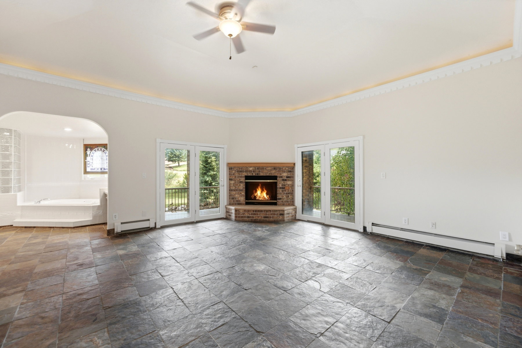 Spacious room featuring slate tile flooring, a corner brick fireplace, and two sets of glass-paned French doors