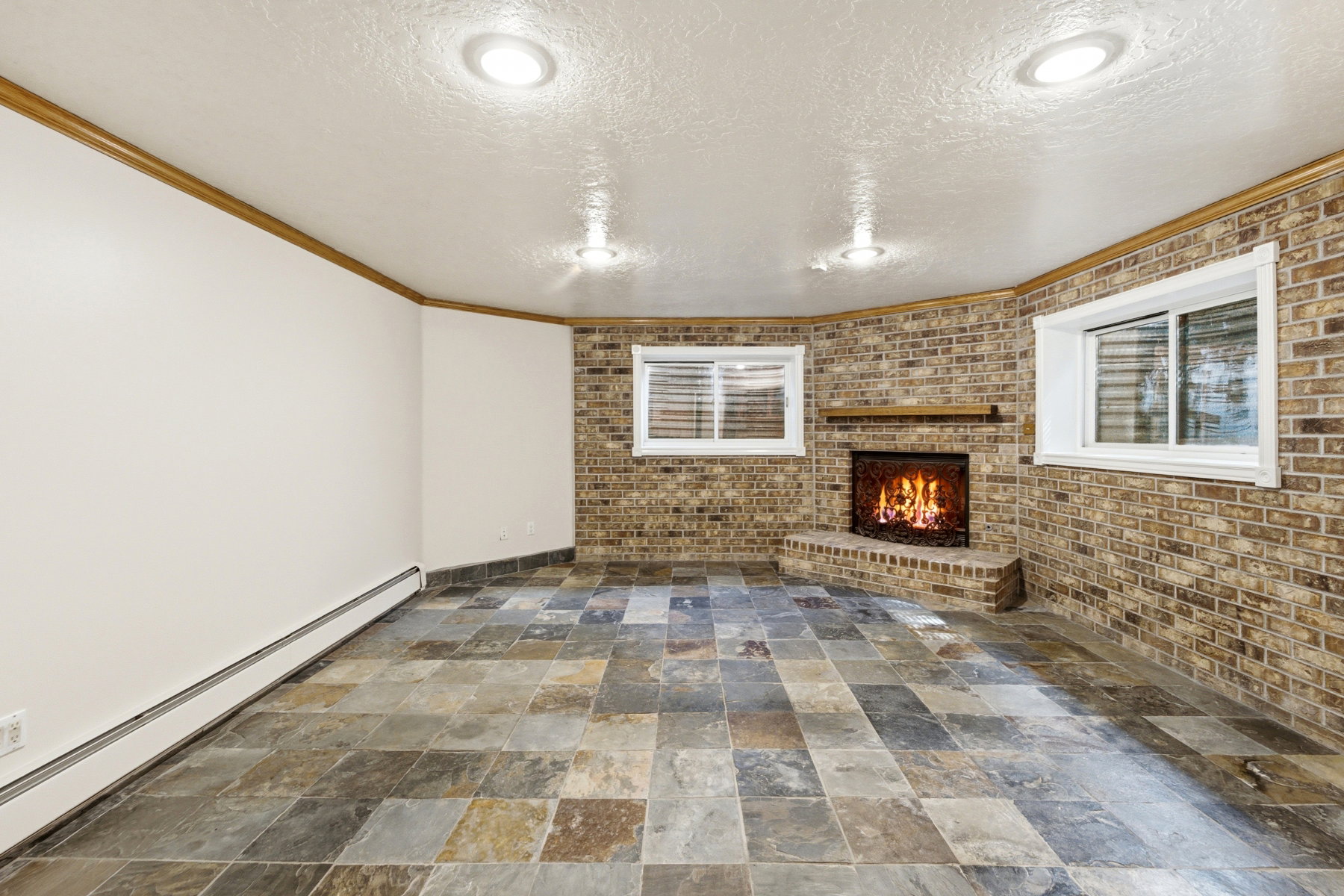 Tile flooring and a corner brick fireplace with a wood mantel
