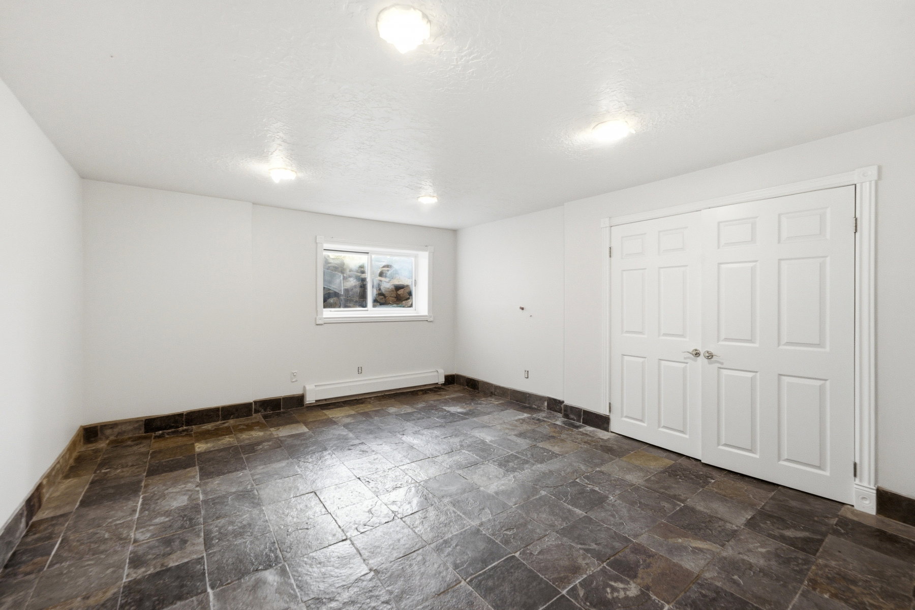 Spacious room featuring slate-style tile flooring, white walls, and a window providing natural light