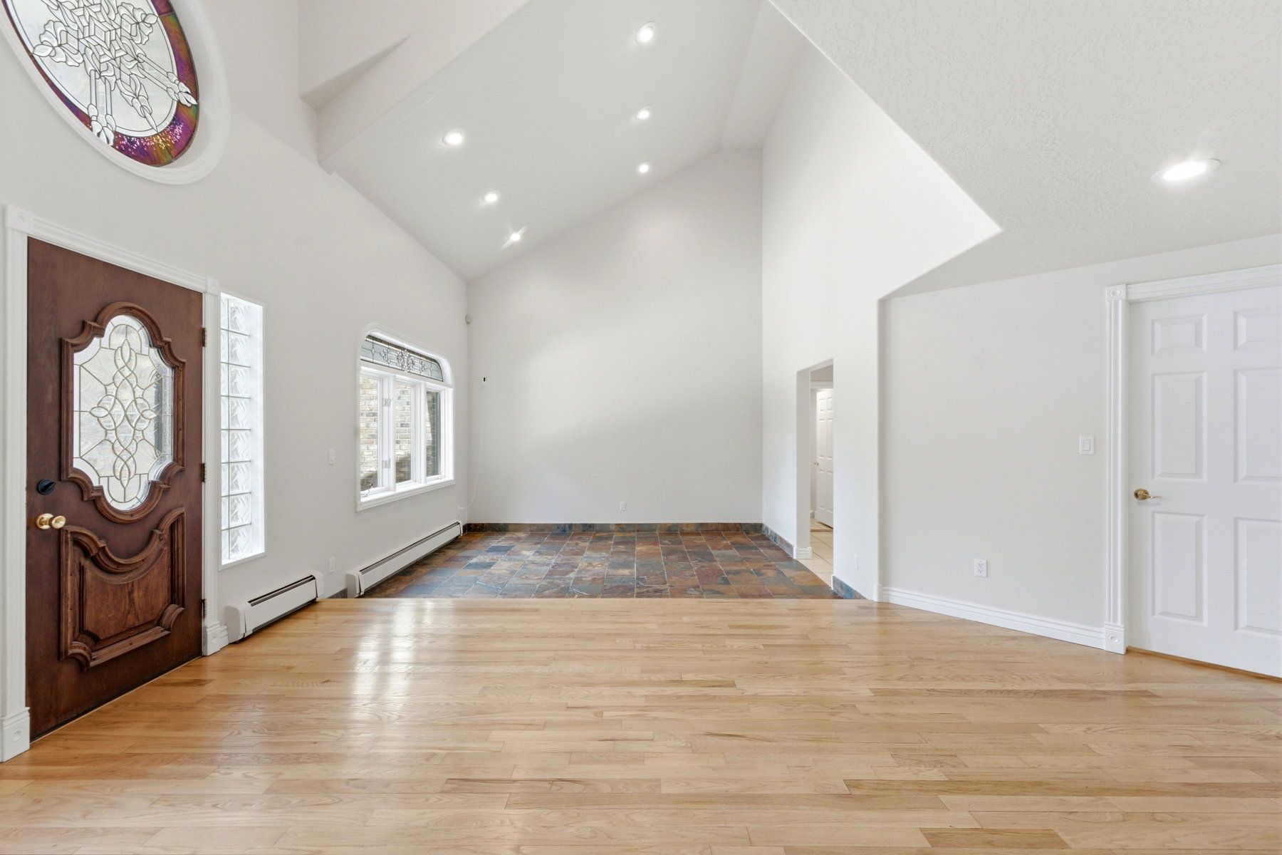 Entry foyer featuring a prominent wood-finish door with decorative glass, an oval stained-glass transom, and high vaulted ceilings with recessed lighting