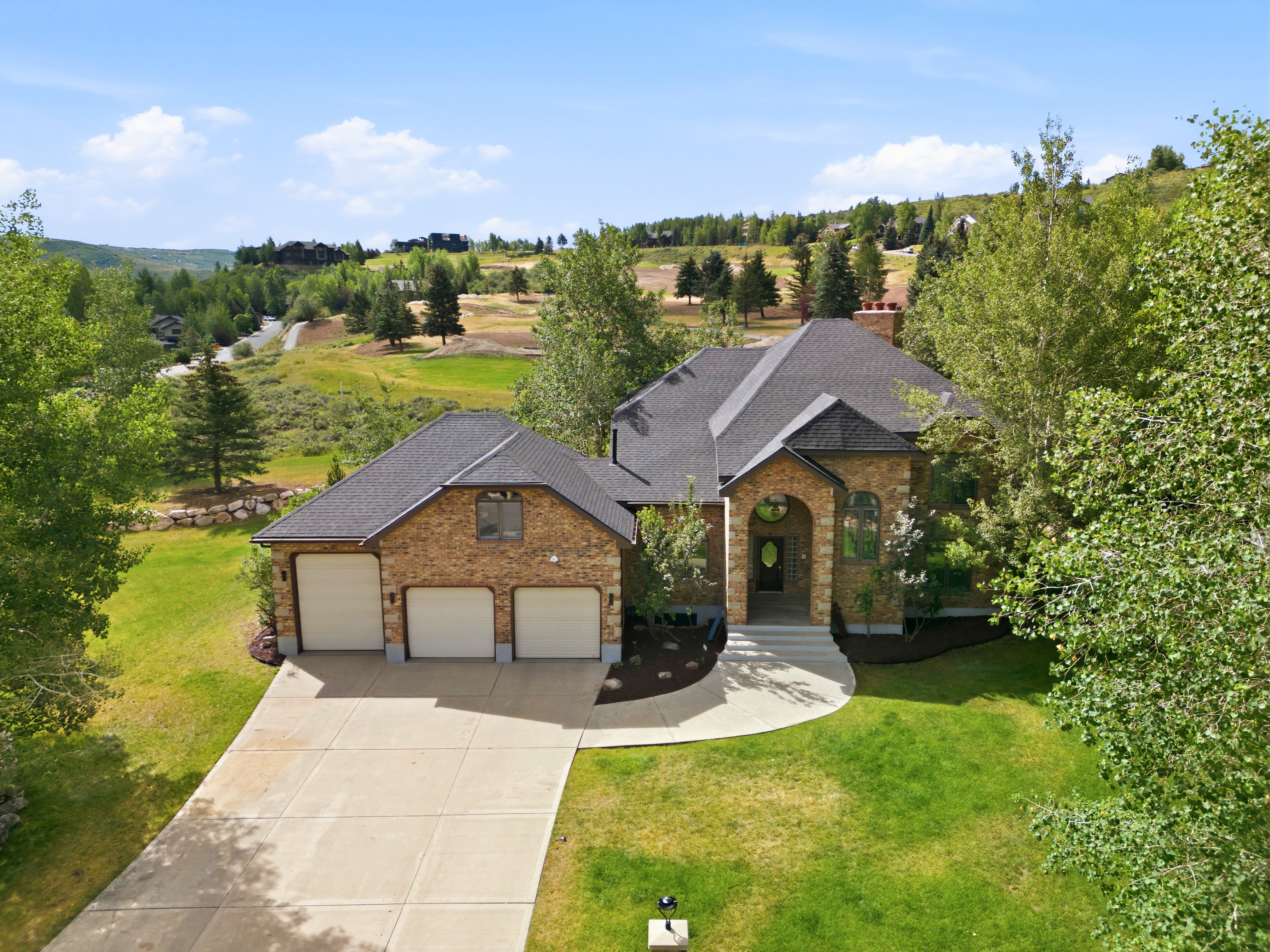 Stone and brick facade residence featuring a multi-car garage, dark shingle roof, arched entry, and a concrete driveway