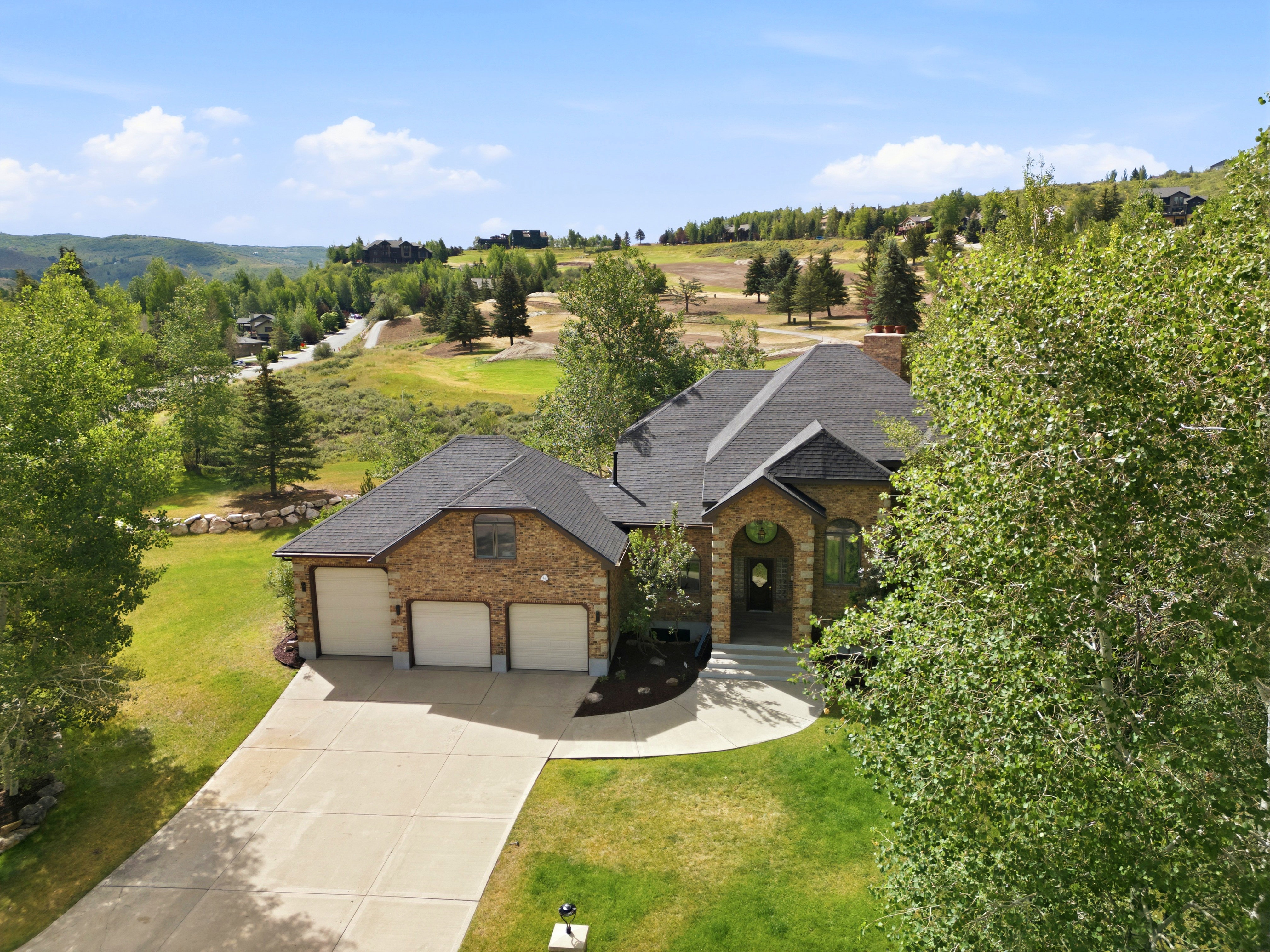 Stone and stucco home featuring a three-car garage, dark shingle roof, arched entryway, and mature landscaping