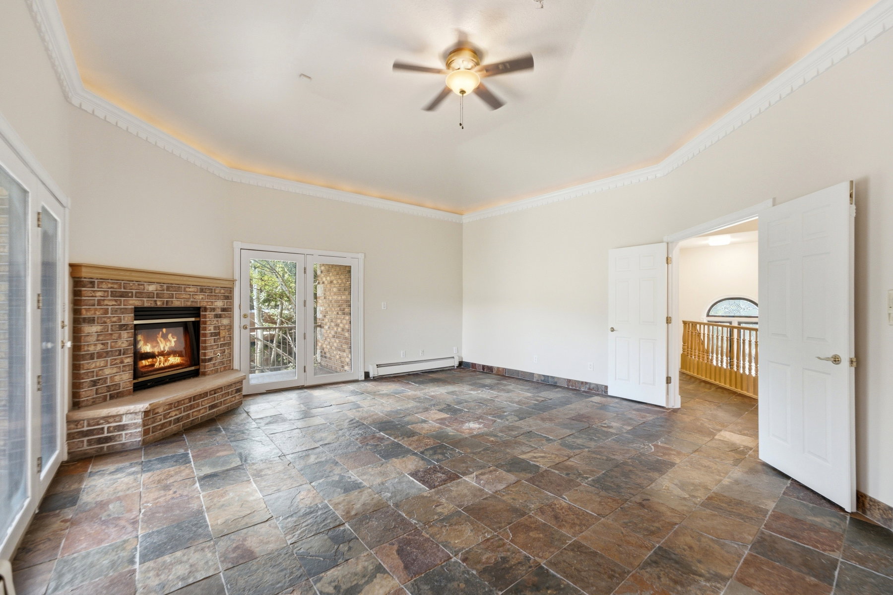 Spacious room featuring slate tile flooring, a corner brick fireplace, and dual French doors leading to exterior access