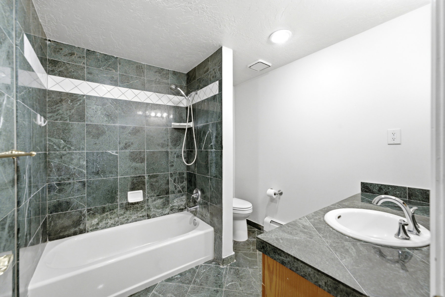 Full bathroom featuring a tiled shower-tub combination with a decorative band, a white porcelain tub, and an integrated shower head