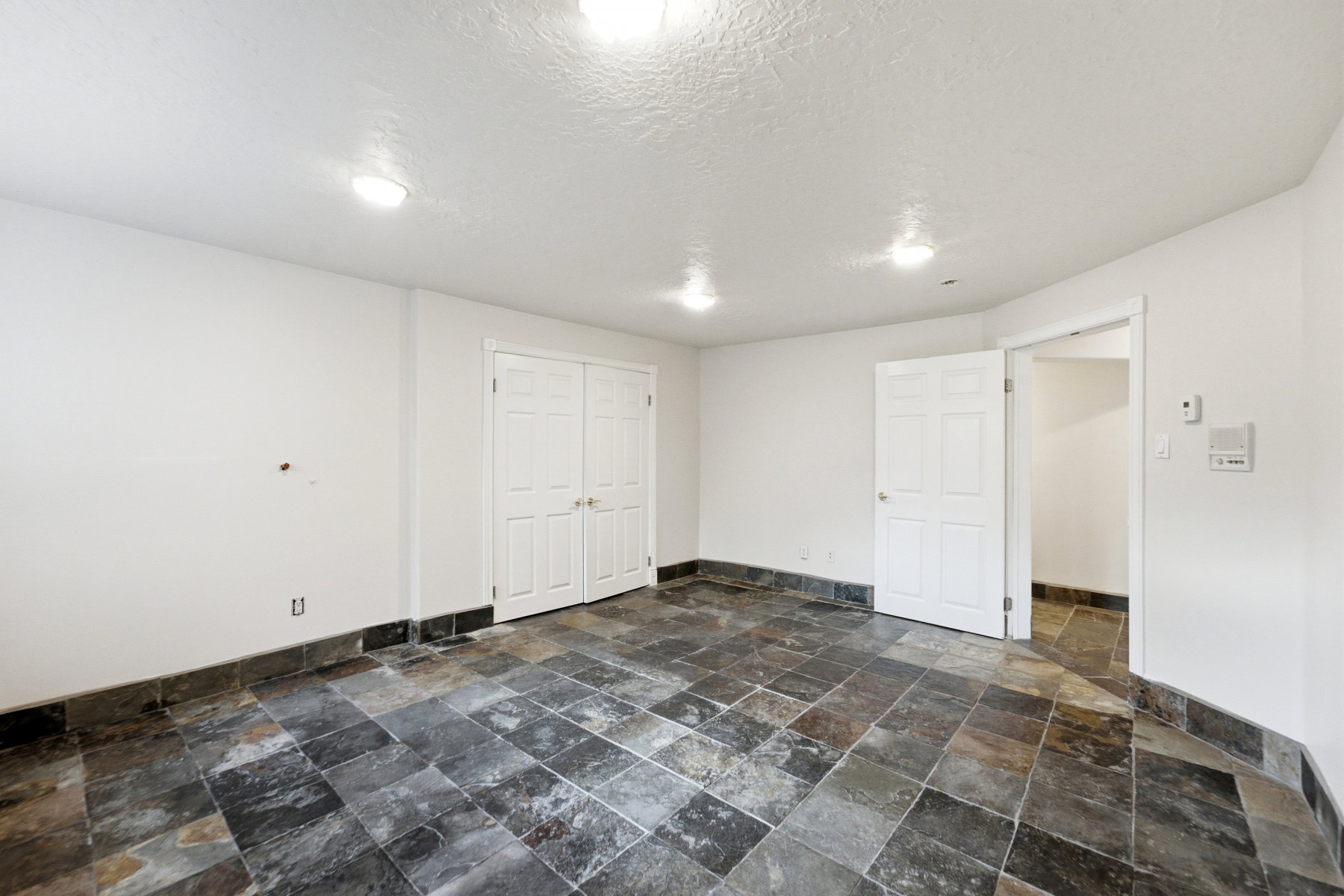 Spacious room featuring slate-style floor tiling, white walls, and built-in ceiling lighting