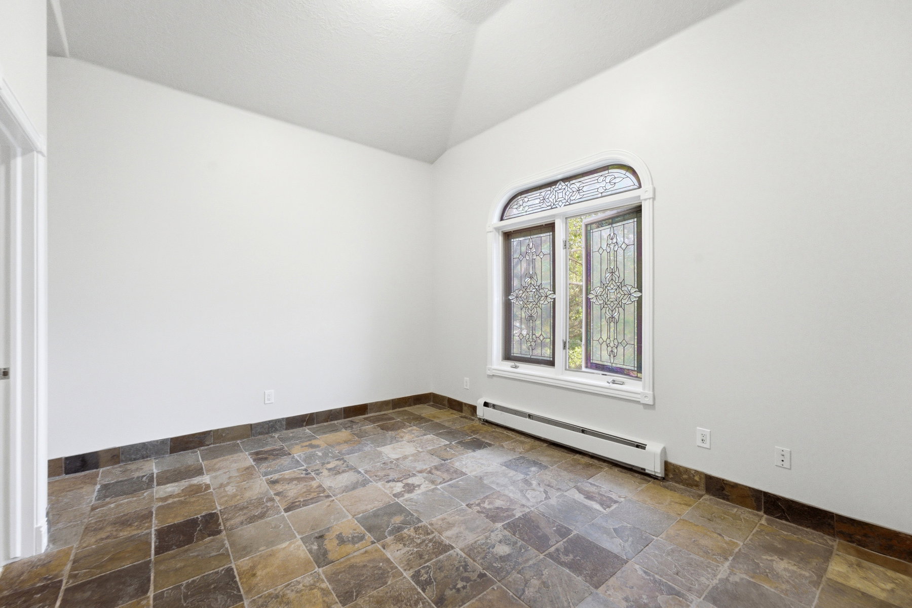 Vaulted ceiling room featuring a stained glass arched window, tile flooring, and white baseboards