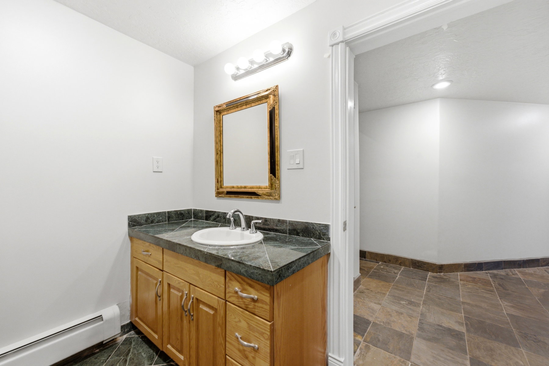 Bathroom vanity featuring a light wood cabinet, dark stone countertop, and a white undermount sink