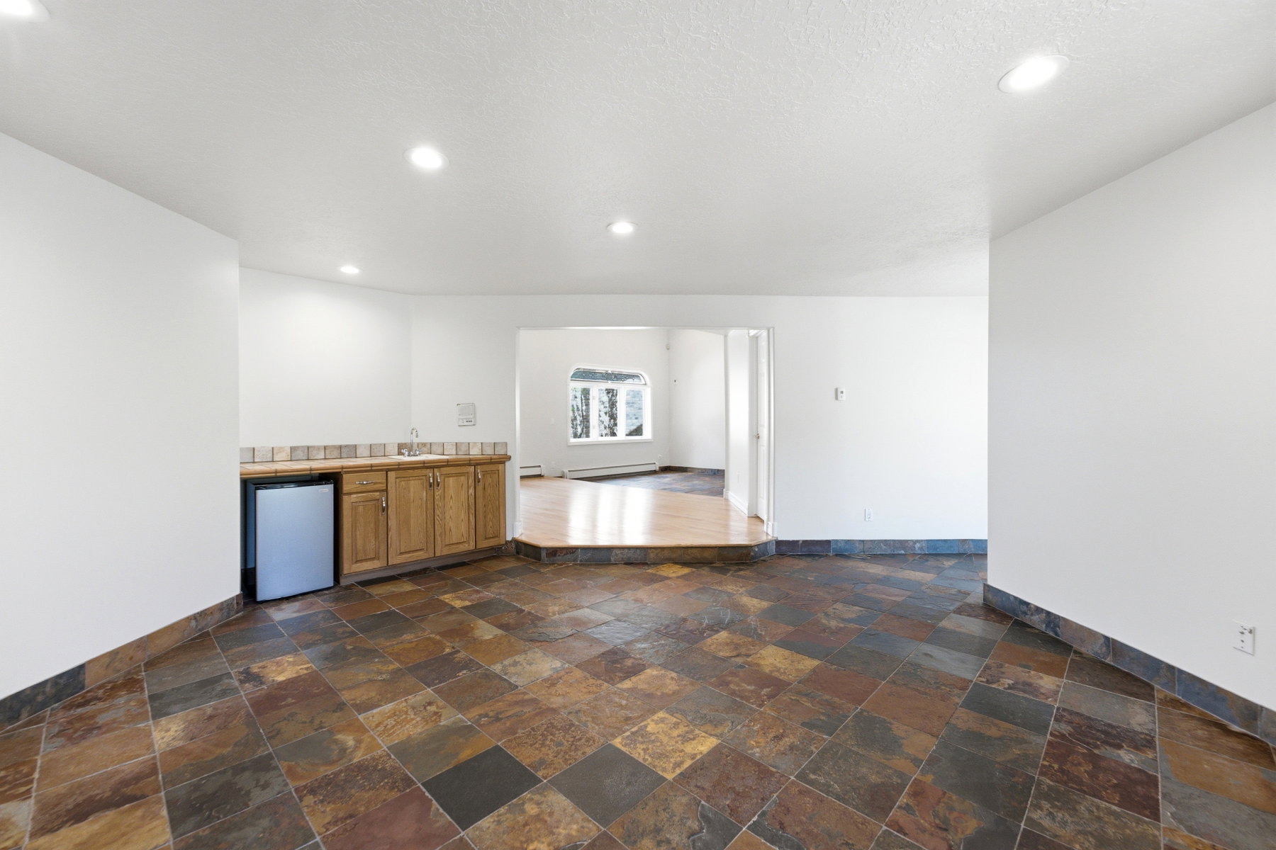 Spacious lower level featuring multicolor slate tile flooring and a built-in wet bar with wood cabinetry, a sink, and a compact refrigerator