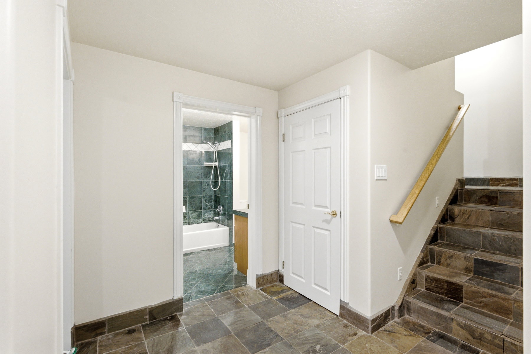 Stone tile flooring with a matching staircase, light wood handrail, and white paneled doors