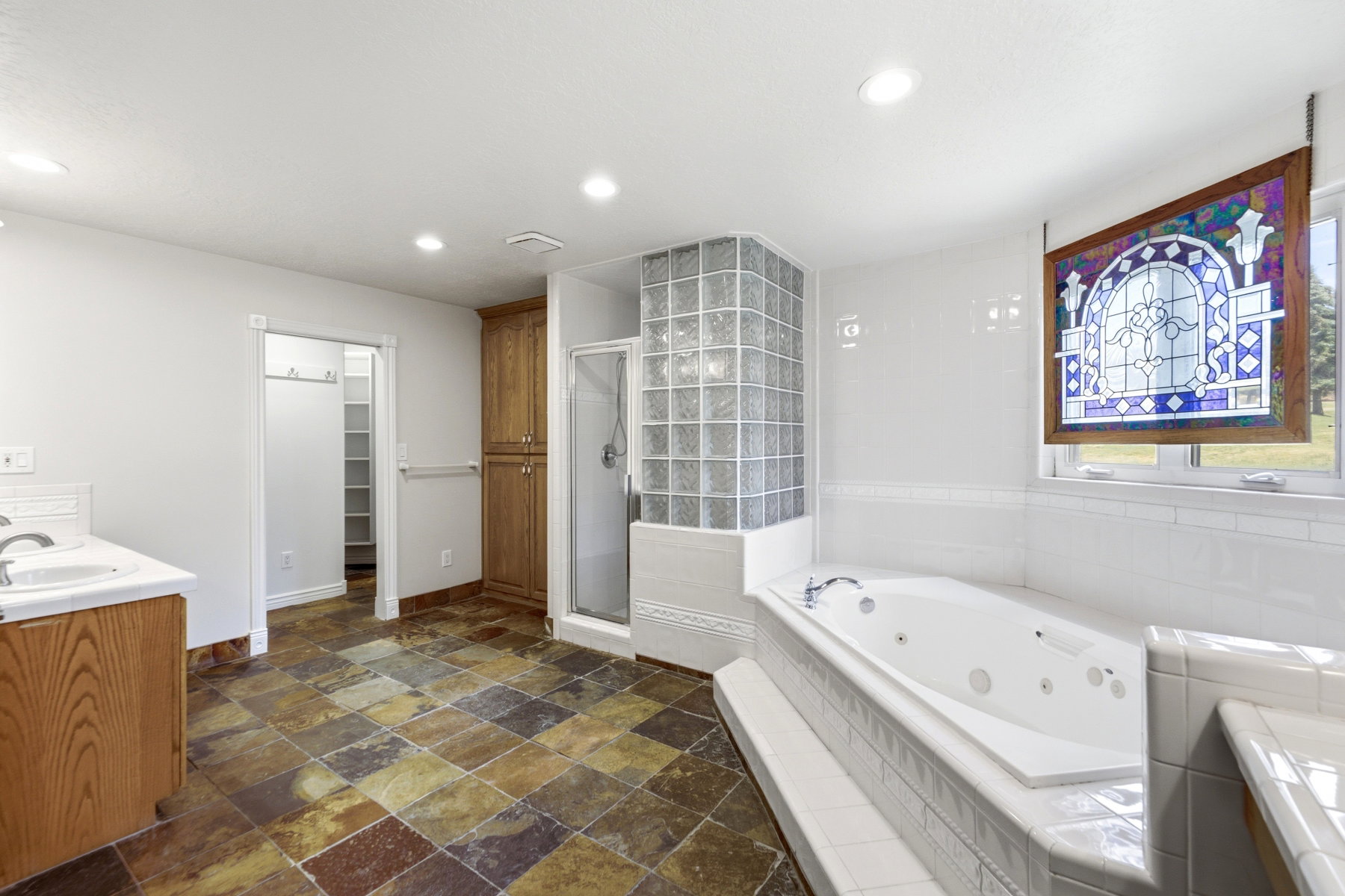 Spacious bathroom featuring a built-in jetted tub, a glass block shower enclosure, and a stained glass window accent