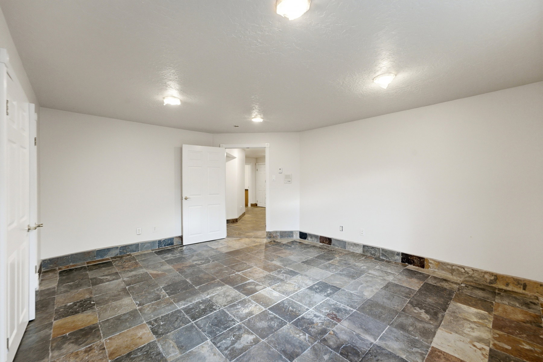 Spacious room featuring slate tile flooring, white walls, and multiple flush-mount ceiling lights