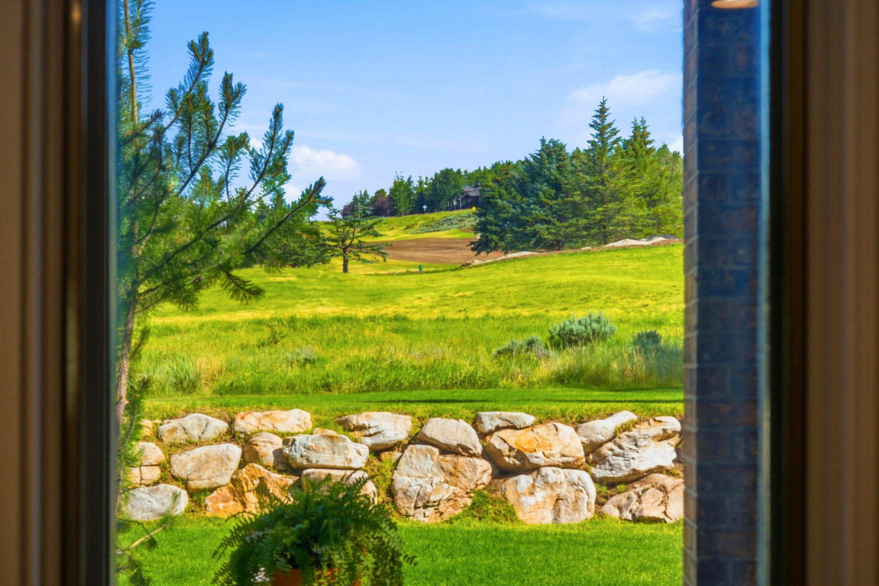 Expansive outdoor landscape featuring rolling hills and distant evergreen trees, bordered by a substantial stone retaining wall
