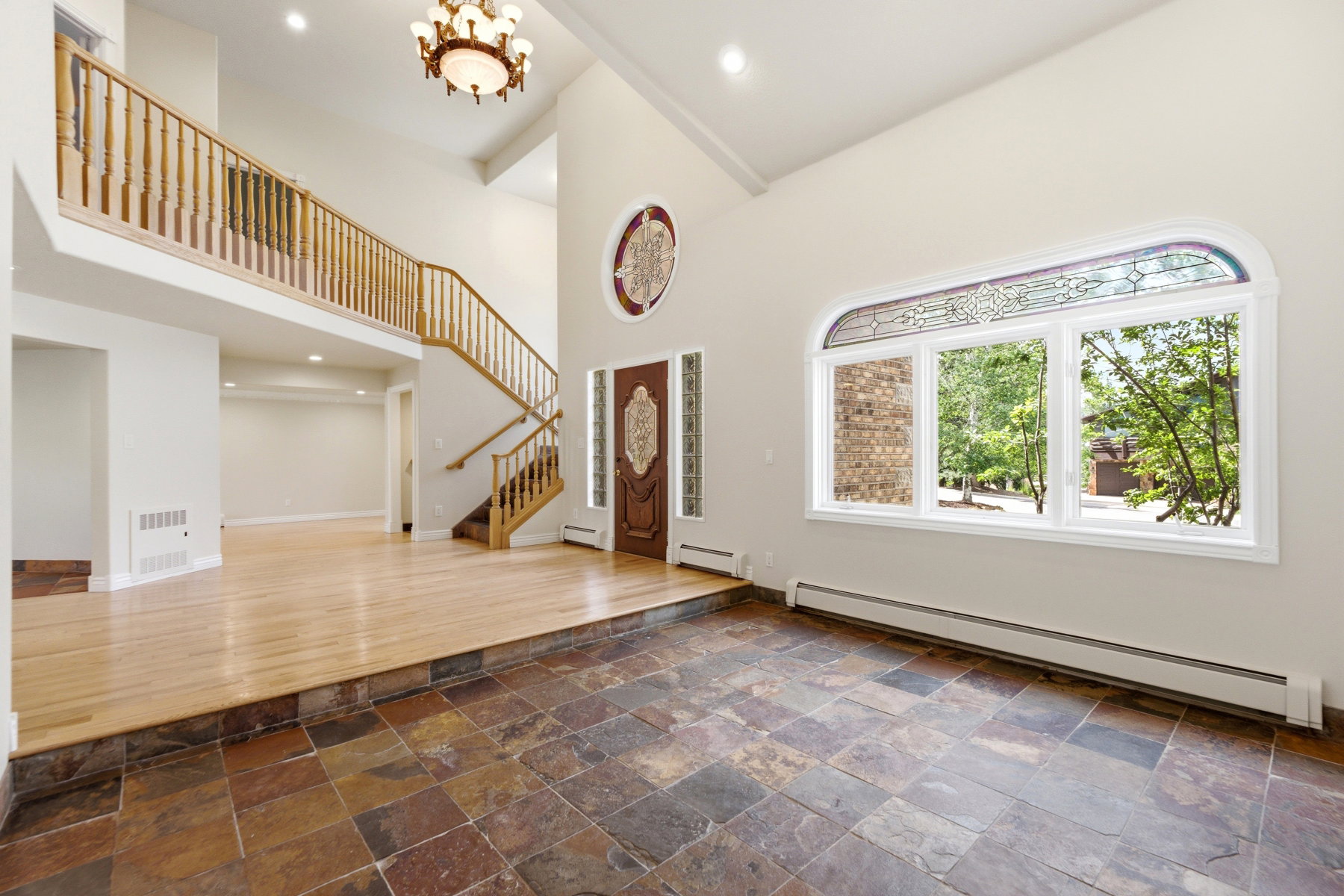 Two-story foyer featuring natural stone tile flooring, a grand staircase with wood railing, high ceilings, a decorative arched stained-glass window, and a wood entry door with ornate glass detailing