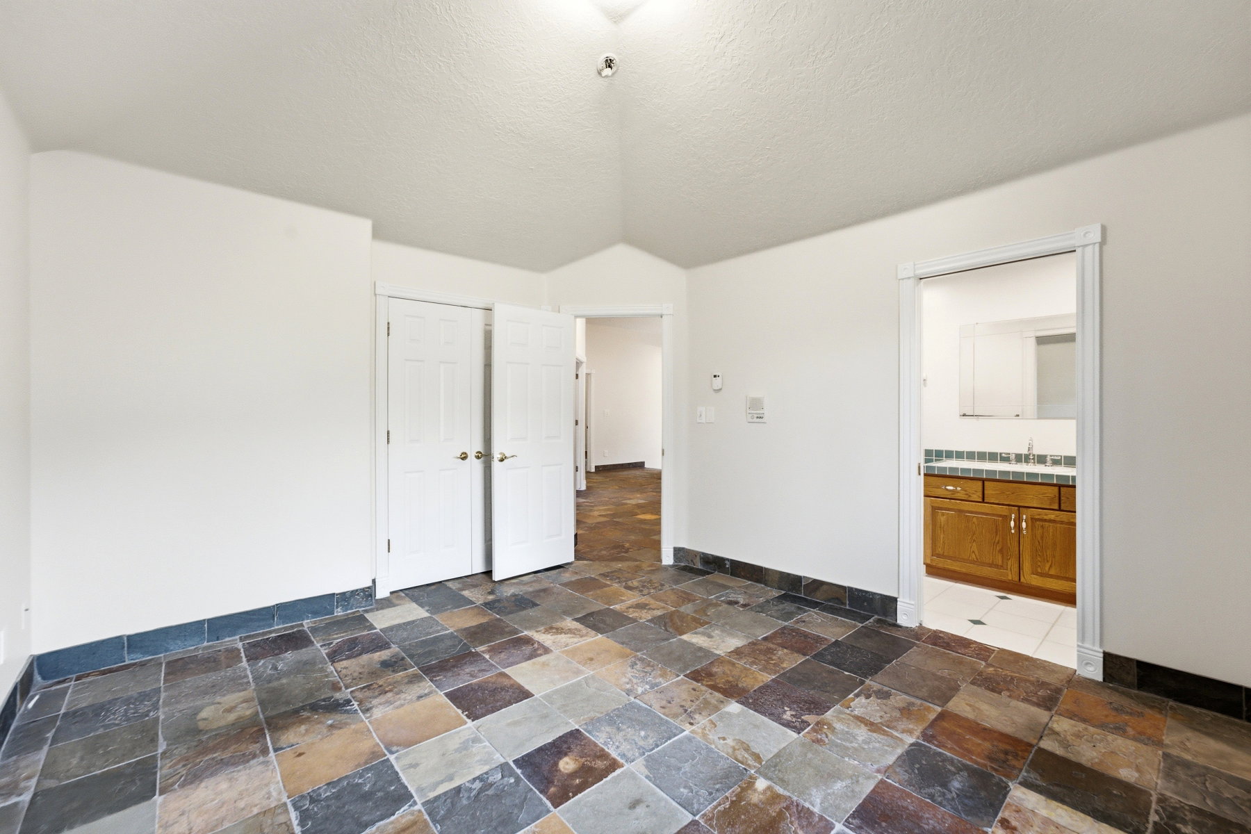 Spacious room featuring multi-toned slate tile flooring, white walls, and a vaulted ceiling