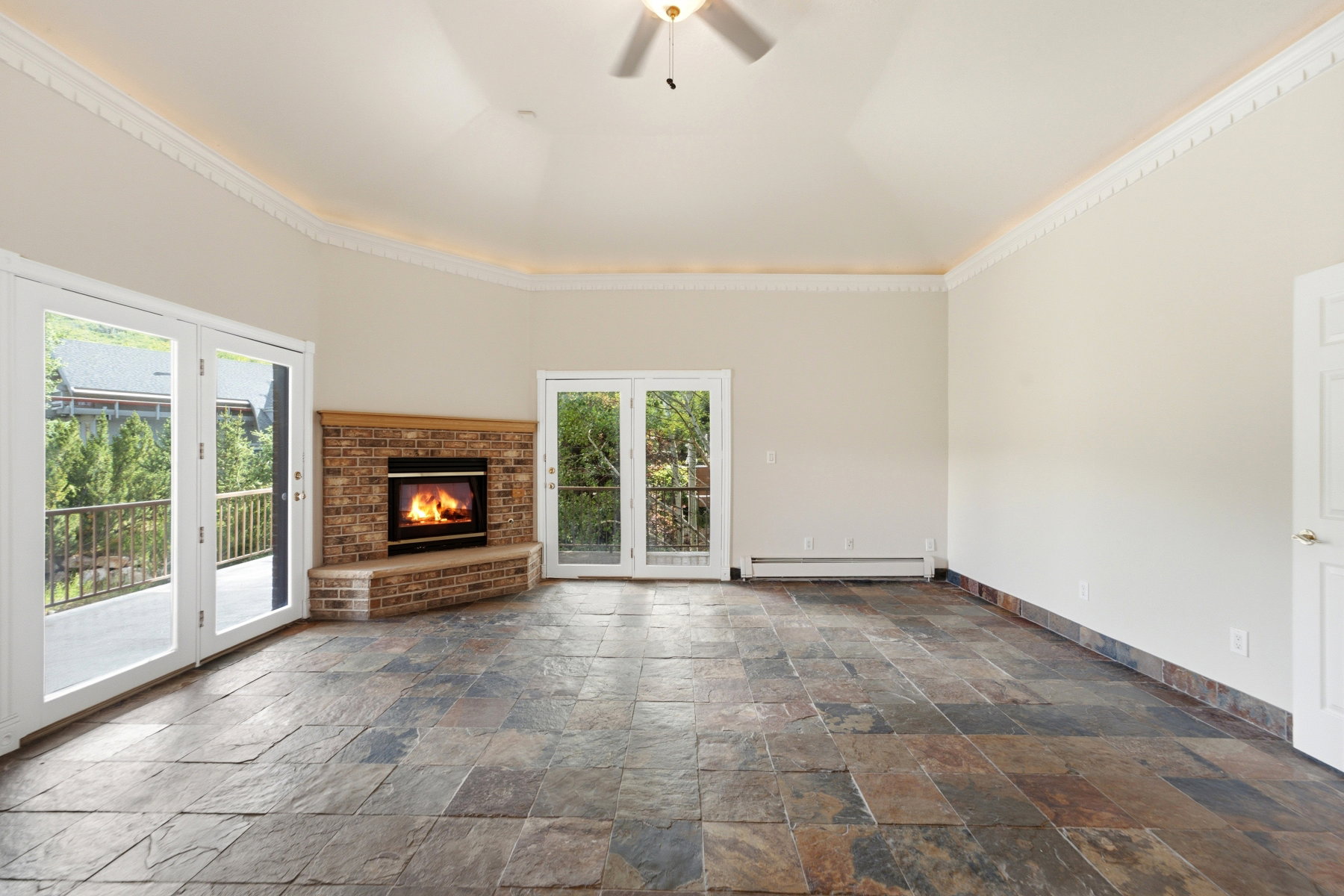 Spacious interior featuring natural stone tile flooring, a brick fireplace with a wood mantle, and multiple sets of glass French doors opening to outdoor spaces