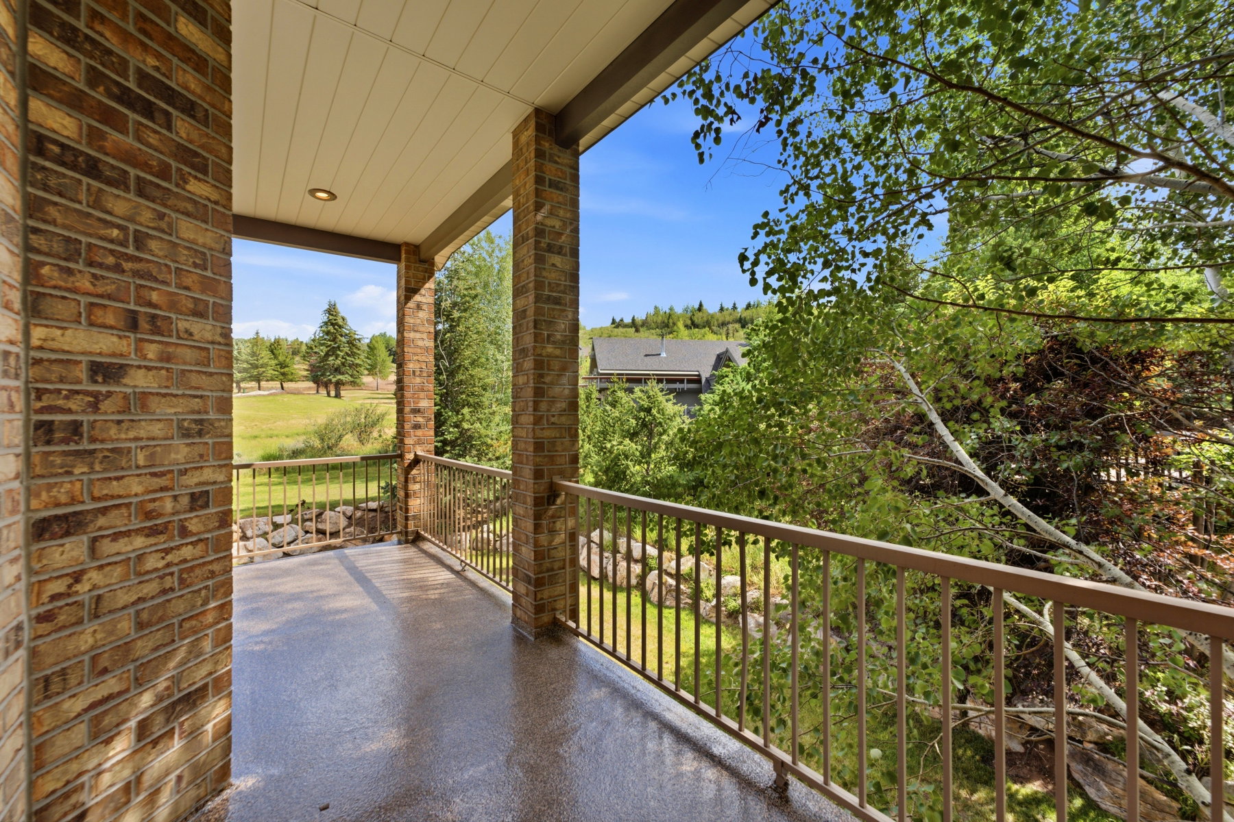 Covered balcony featuring brick columns, a metal railing, and a textured floor surface