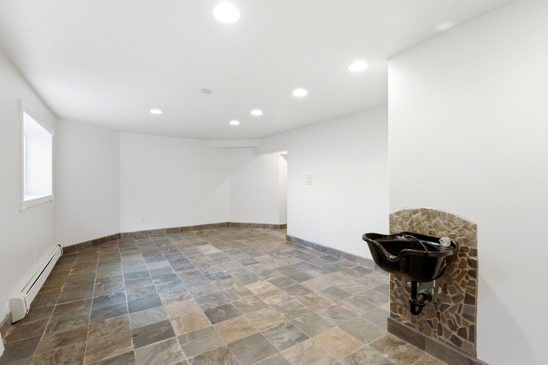 Spacious room featuring slate-style tile flooring, recessed ceiling lighting, a wall-mounted basin with stone tile surround, and white painted walls