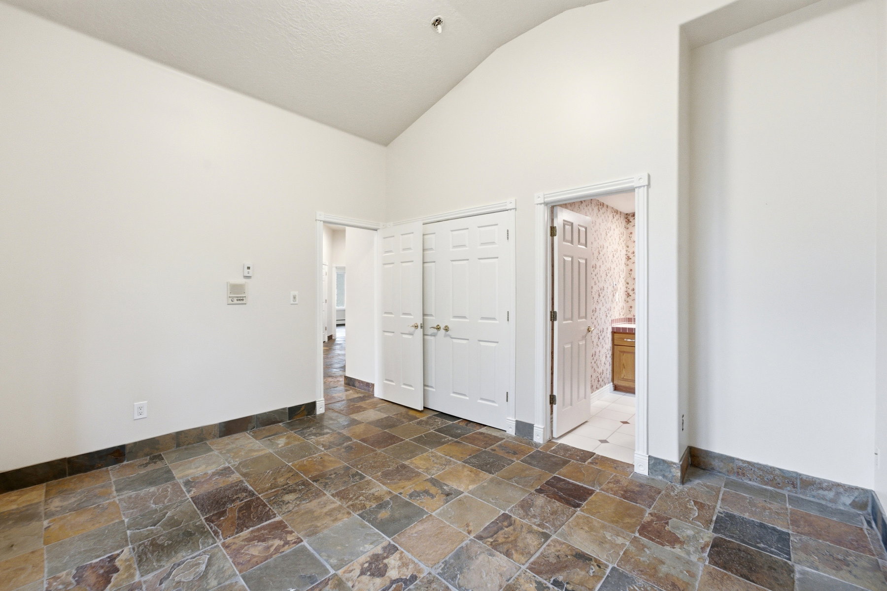 Vaulted ceiling room featuring natural stone tile flooring and a coordinating stone baseboard