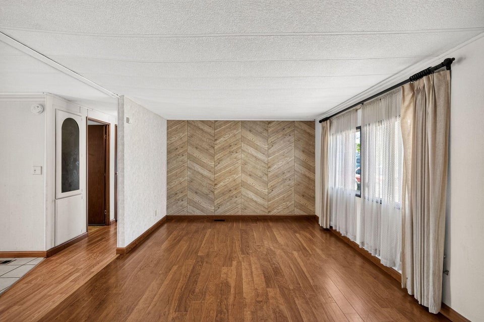 Wood-finish flooring throughout, complemented by a chevron pattern accent wall and a large window with sheers and drapes
