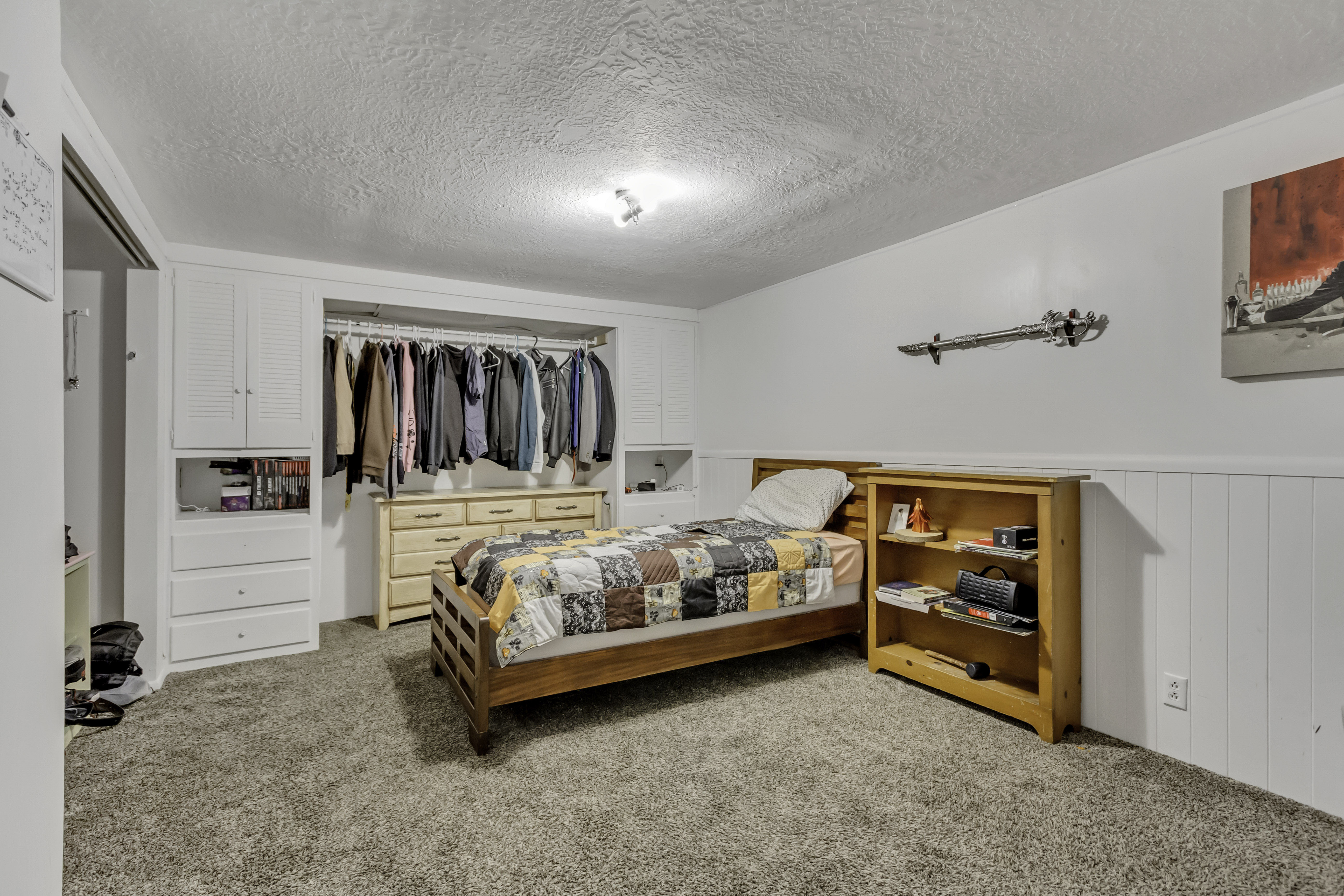 Bedroom featuring built-in white cabinetry, open closet space, white wainscoting, and textured carpeting